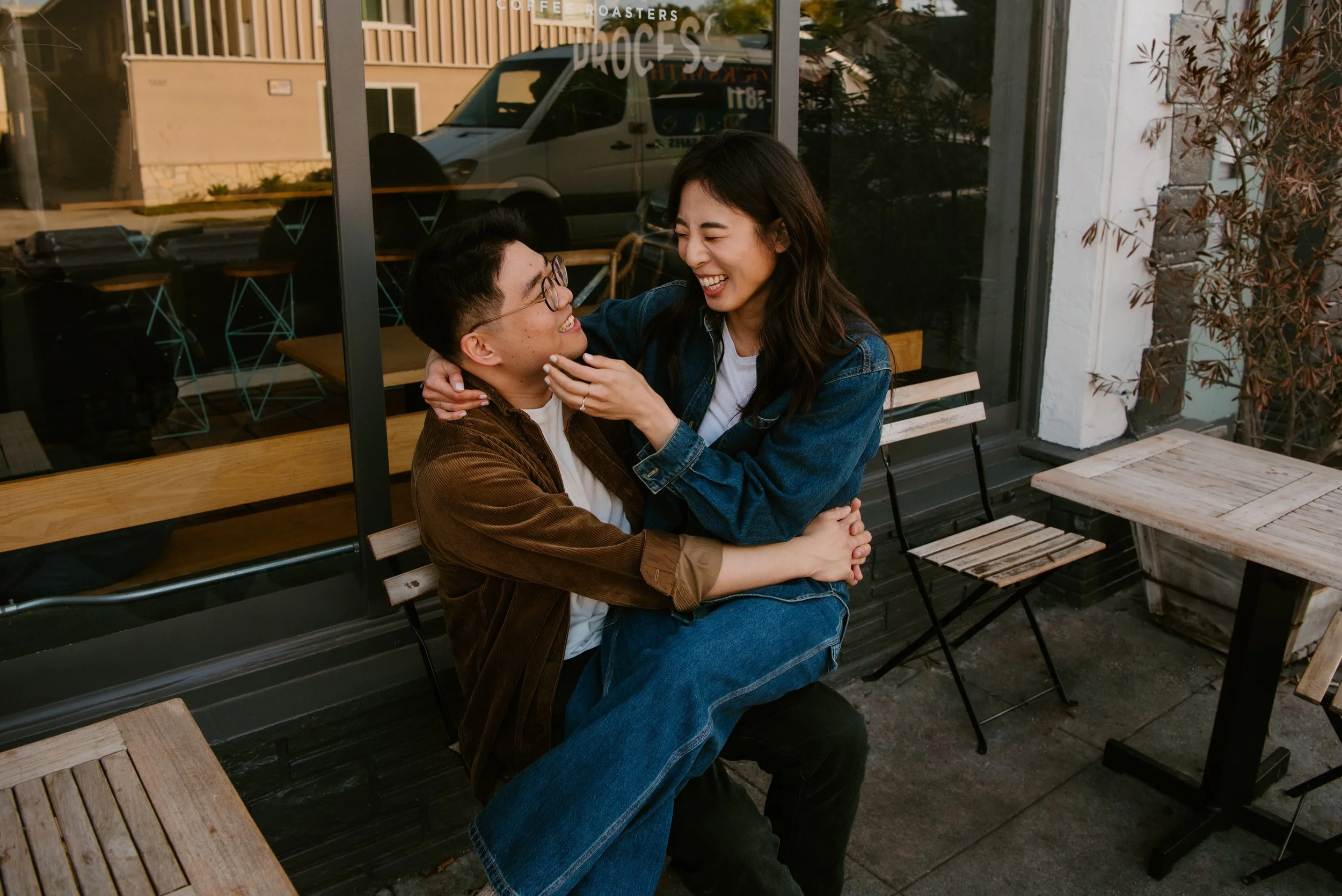 Girl laughing as she sits on guys lap in front of a coffee shop