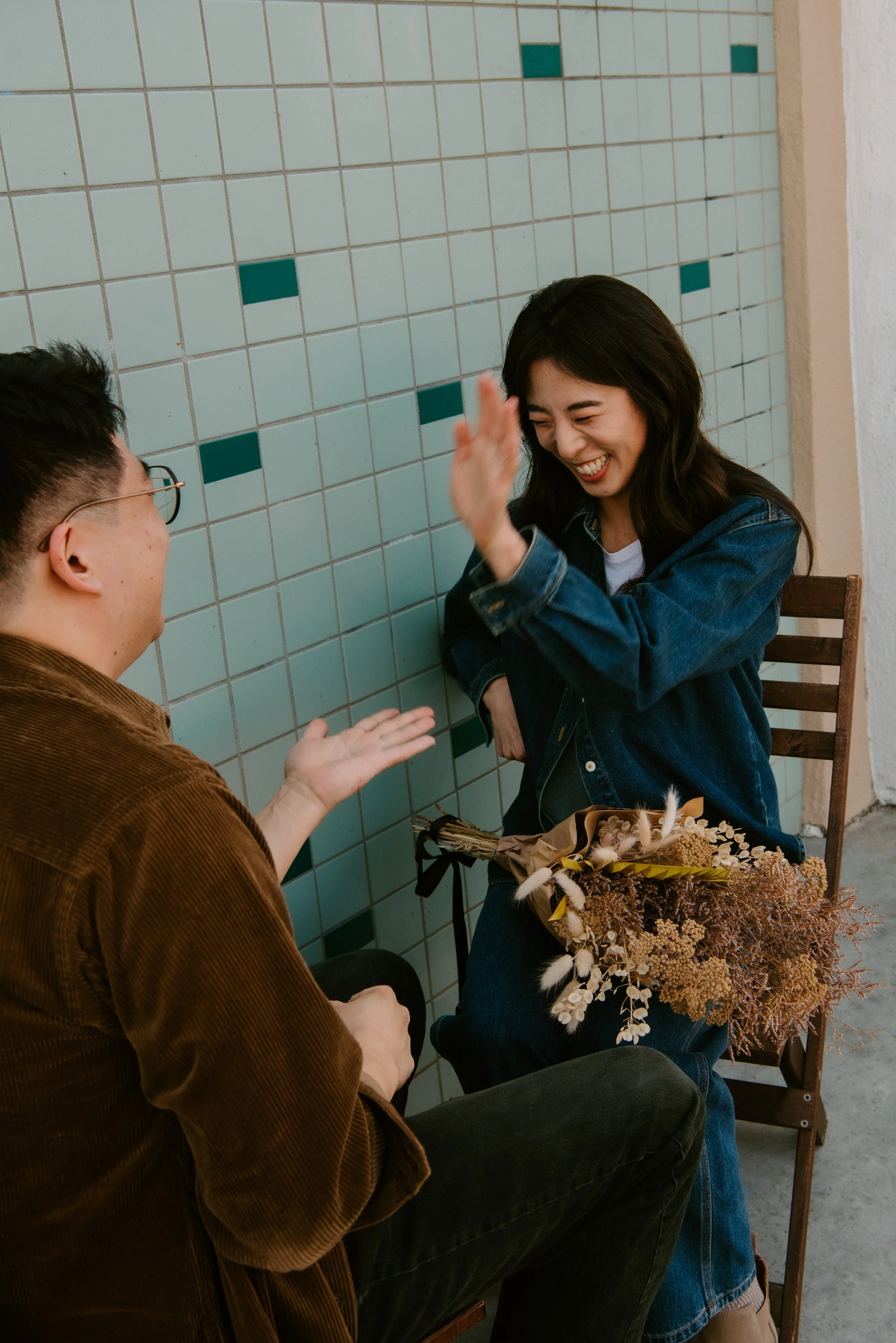 Guy and girl facing each other in chairs. Couple is laughing as they play a hand game