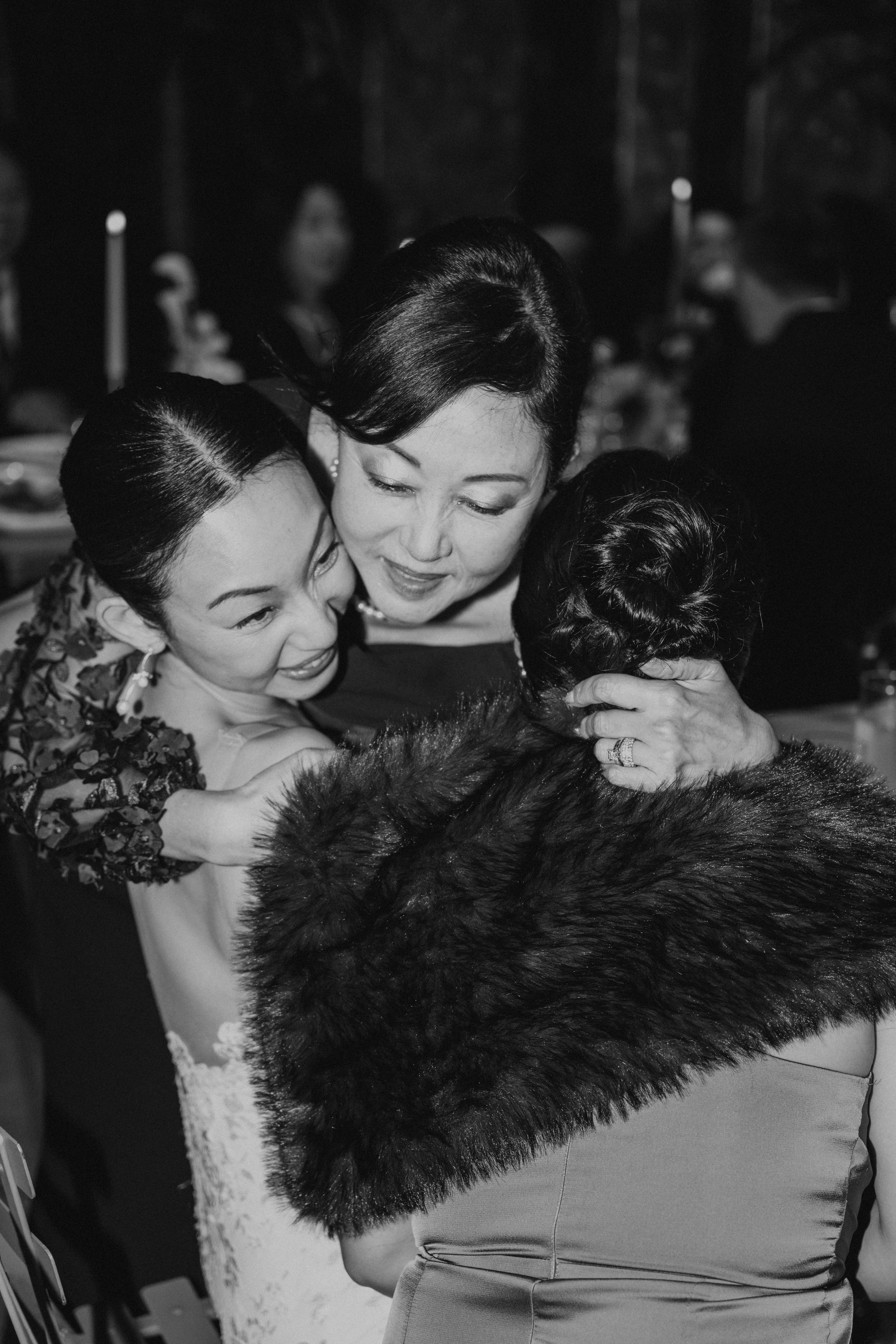Black and white photo of Bride's Mom hugging the bride and a bridesmaid