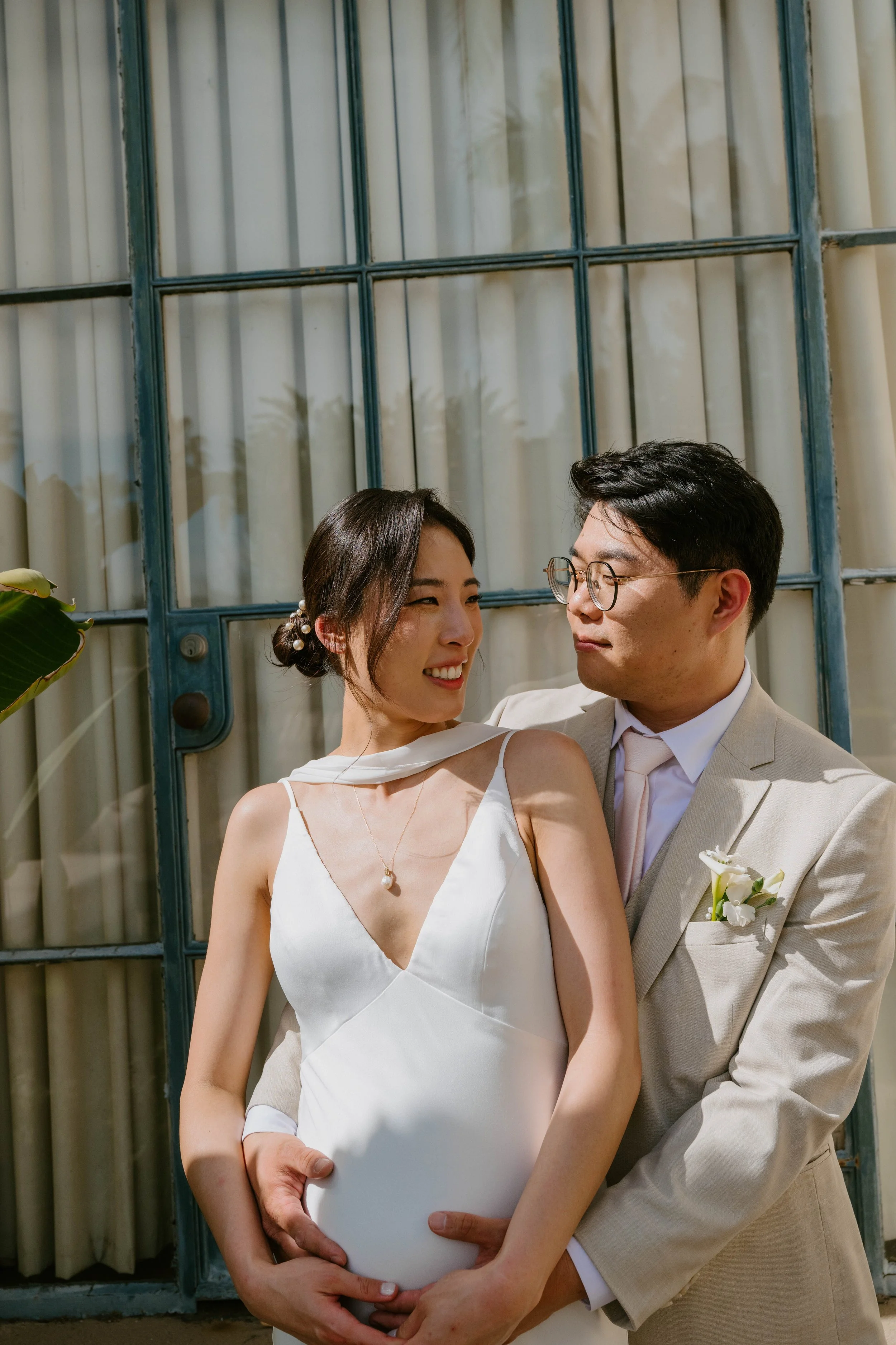 black and white photos of groom standing behind bride with his arms around her. The couple is looking at one another as they hold her belly bump
