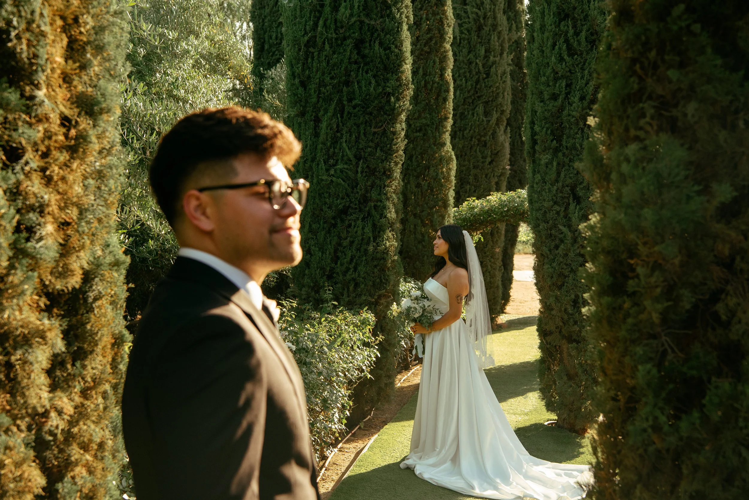 Shot of groom standing close to the camera slightly burry and bride stands farther away in focus