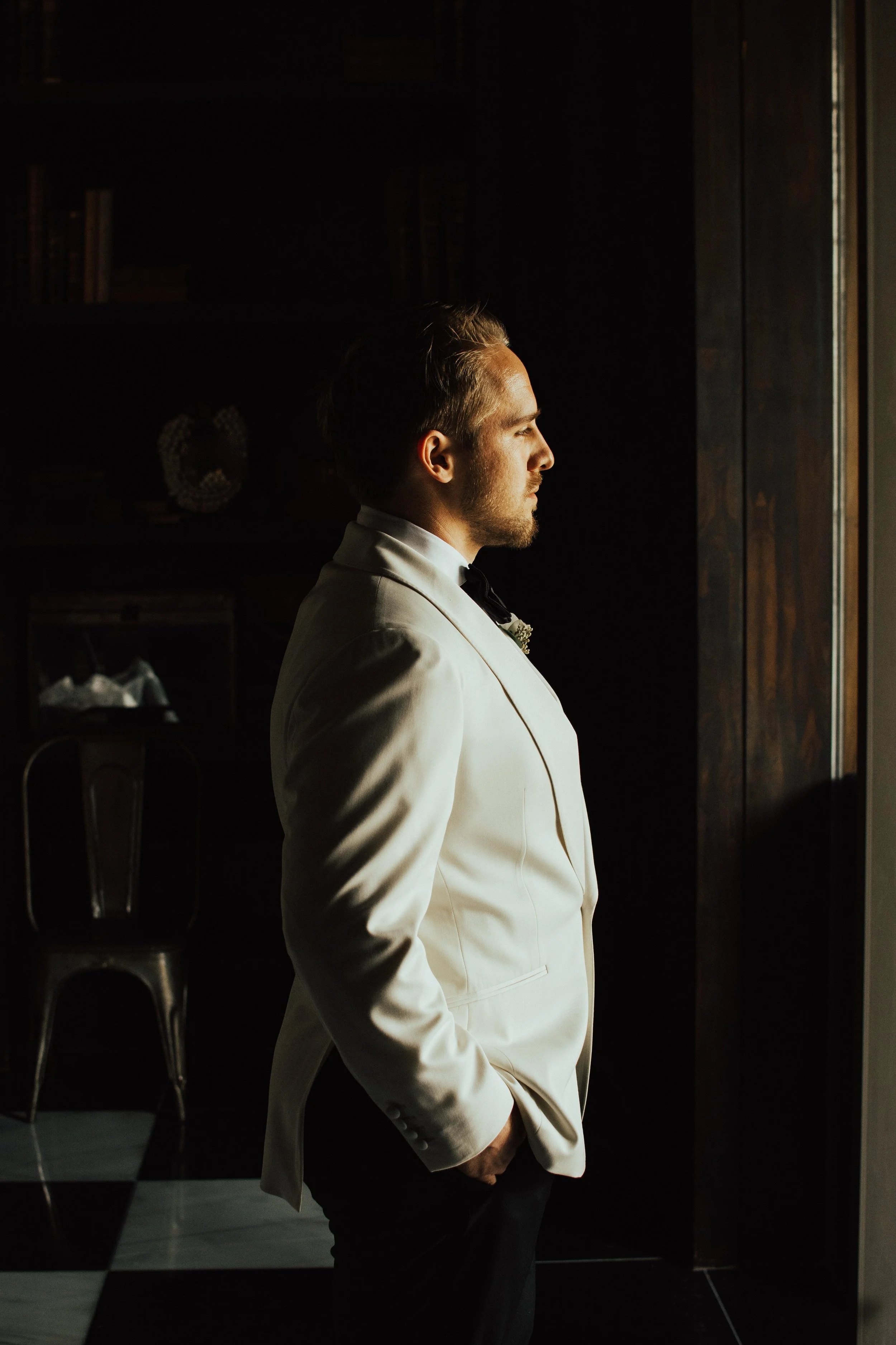 groom standing in white suit jacket looking out a glass door