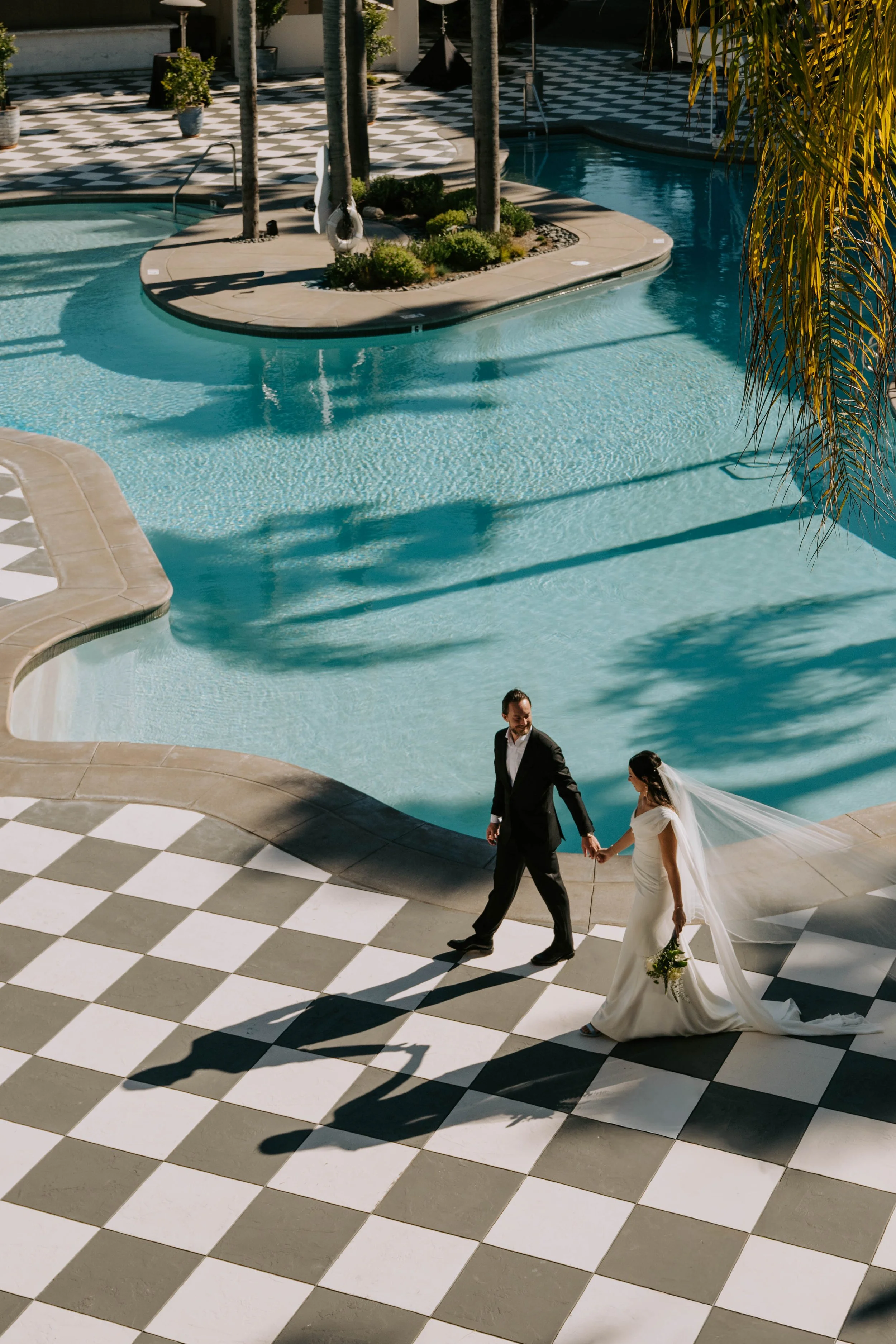 Groom leading Bride on a checkered floor with pool in the background