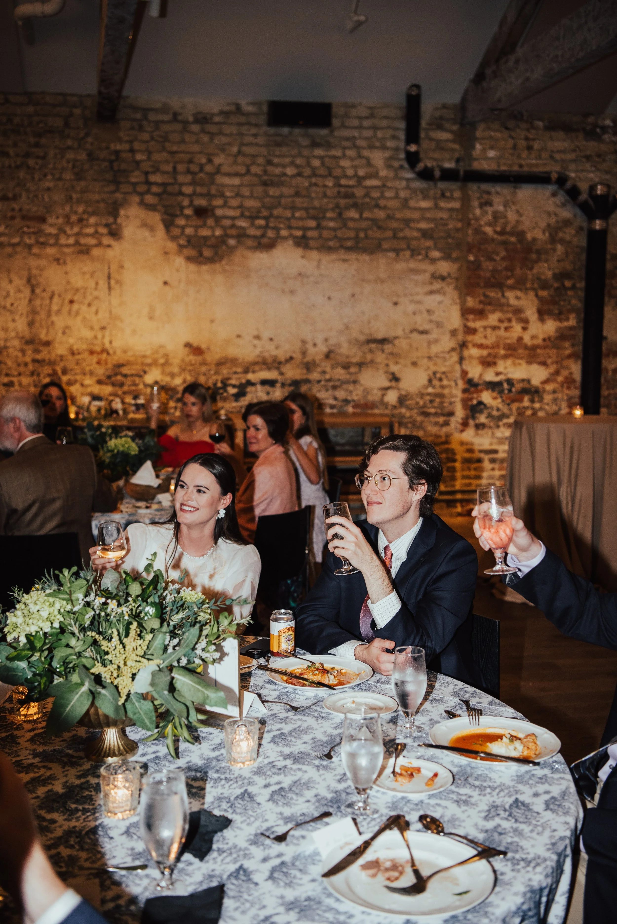 bride and groom sitting at a table raising a glass