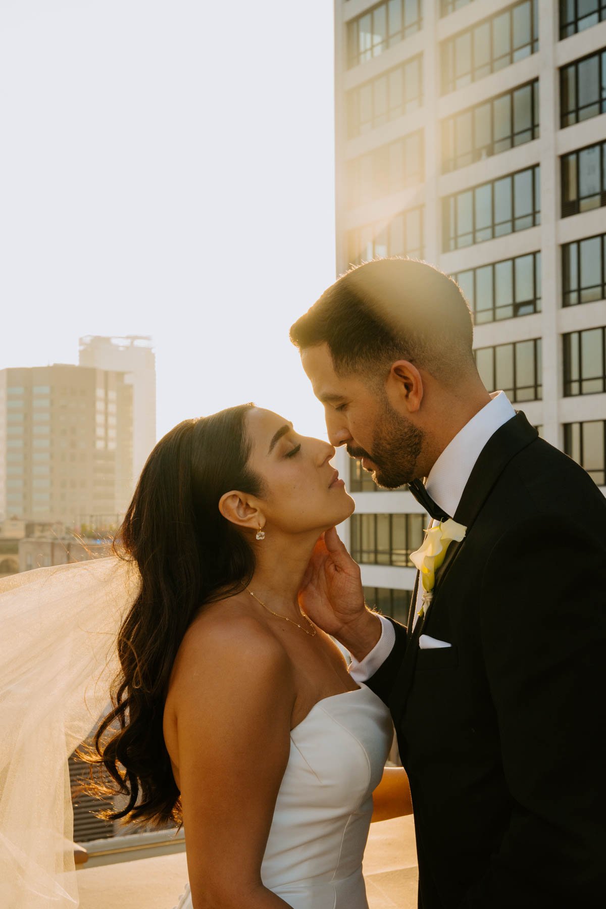 Bride and groom leaning in for a kiss with the sun glowing behind them.