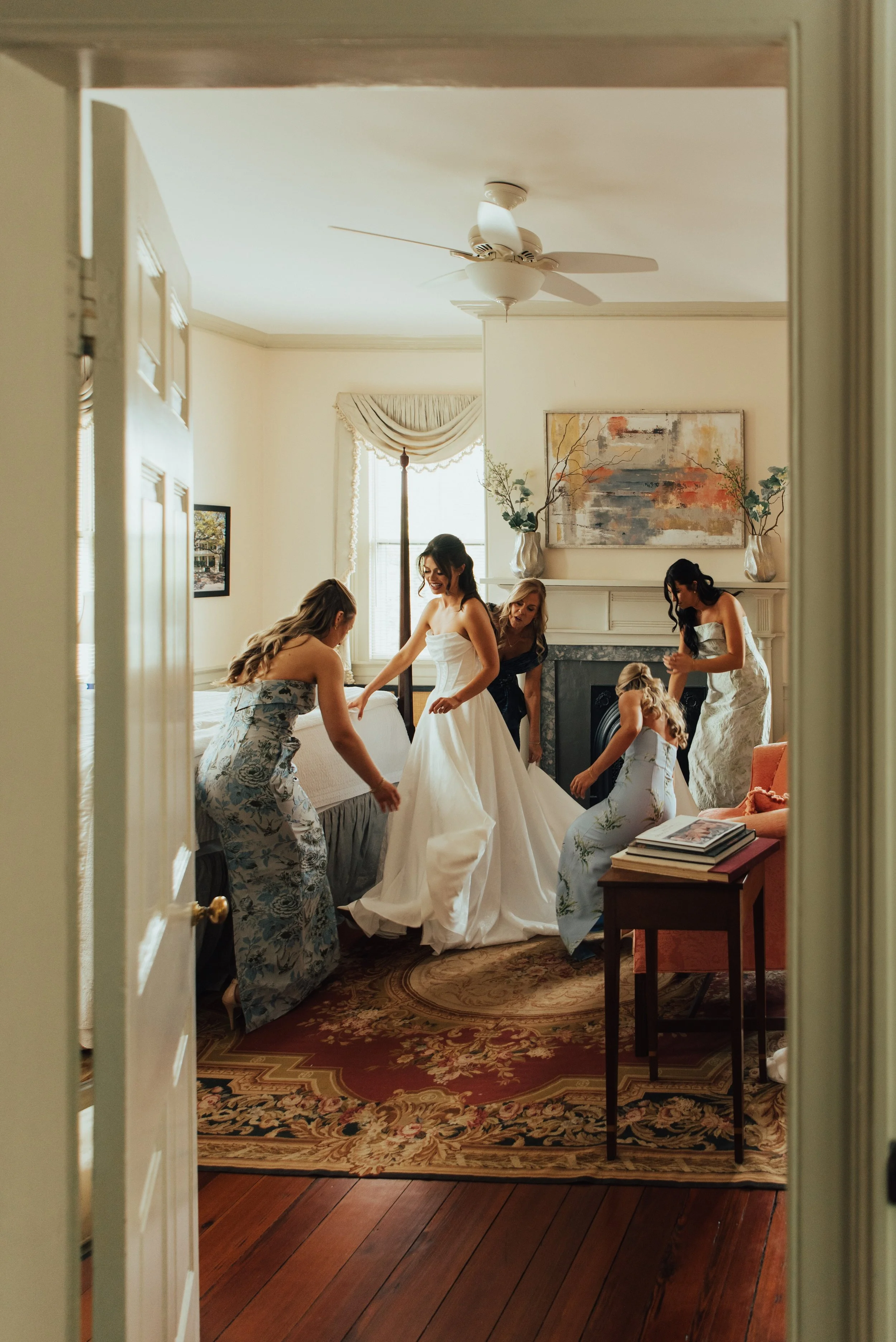 Photo shot through a door way of bridesmaids helping a bride with her dress