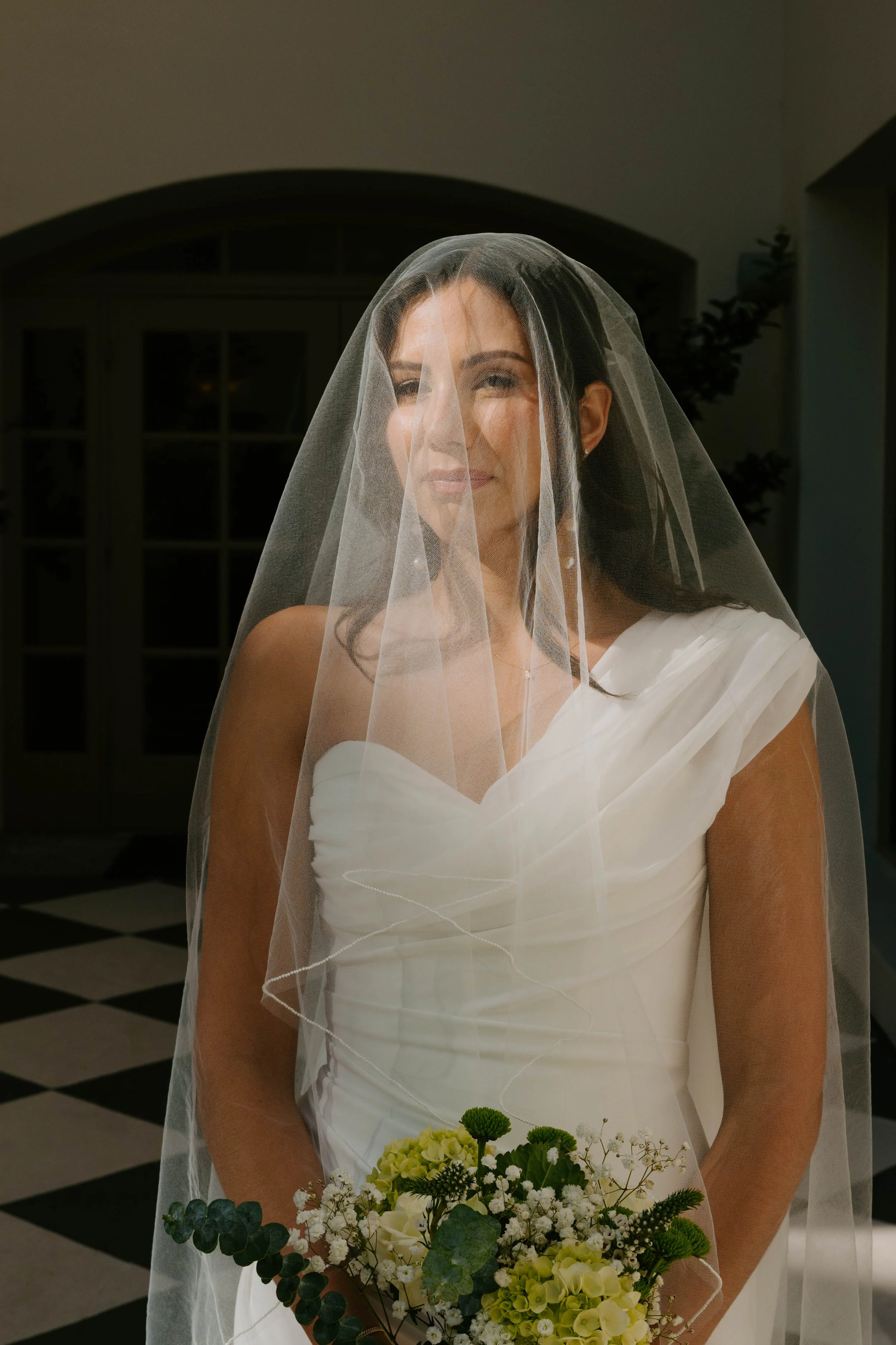 Bride standing in sunlight with veil over her face looking at camera