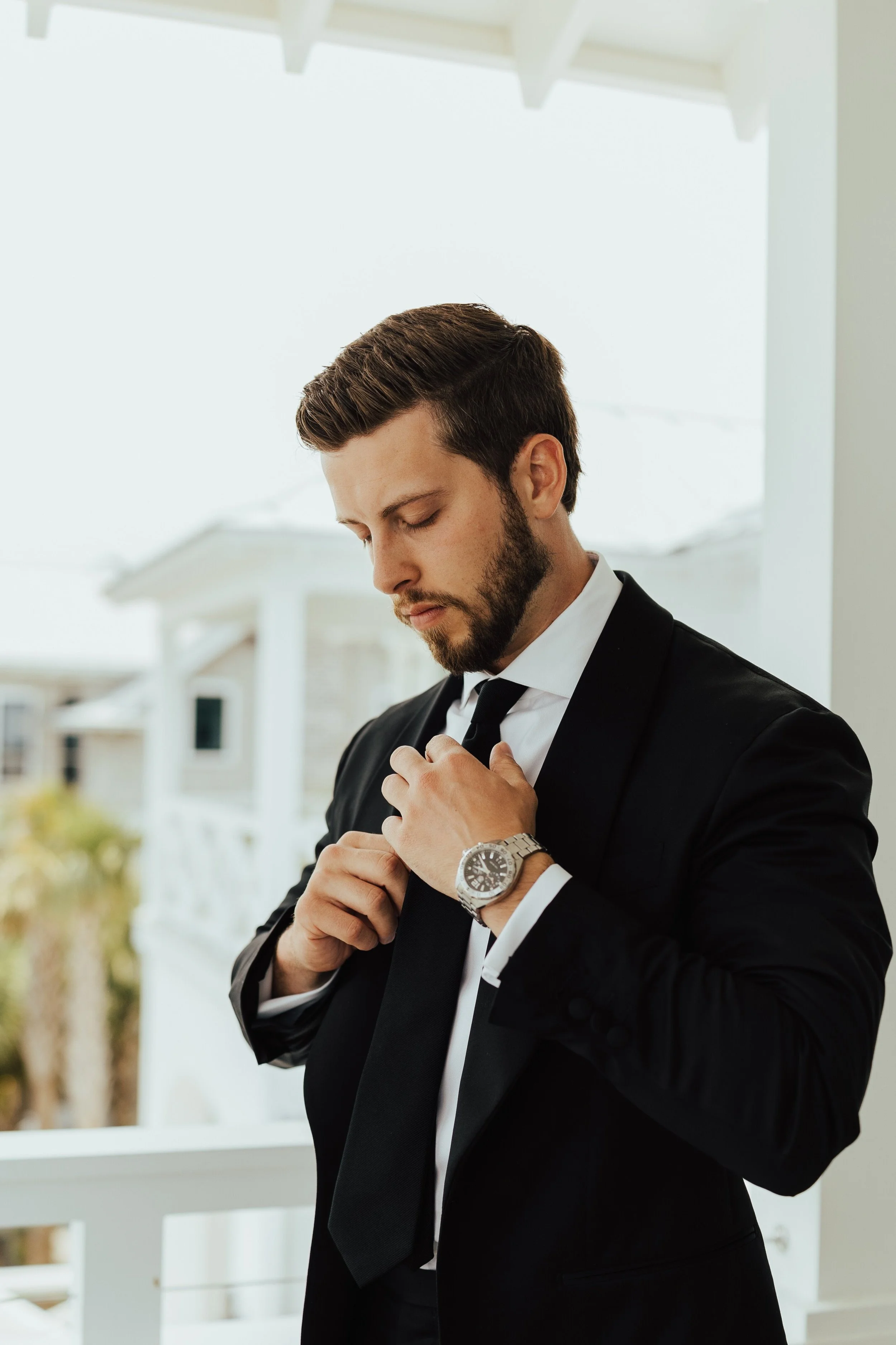Photo of groom adjusting his tie out on a balcony.