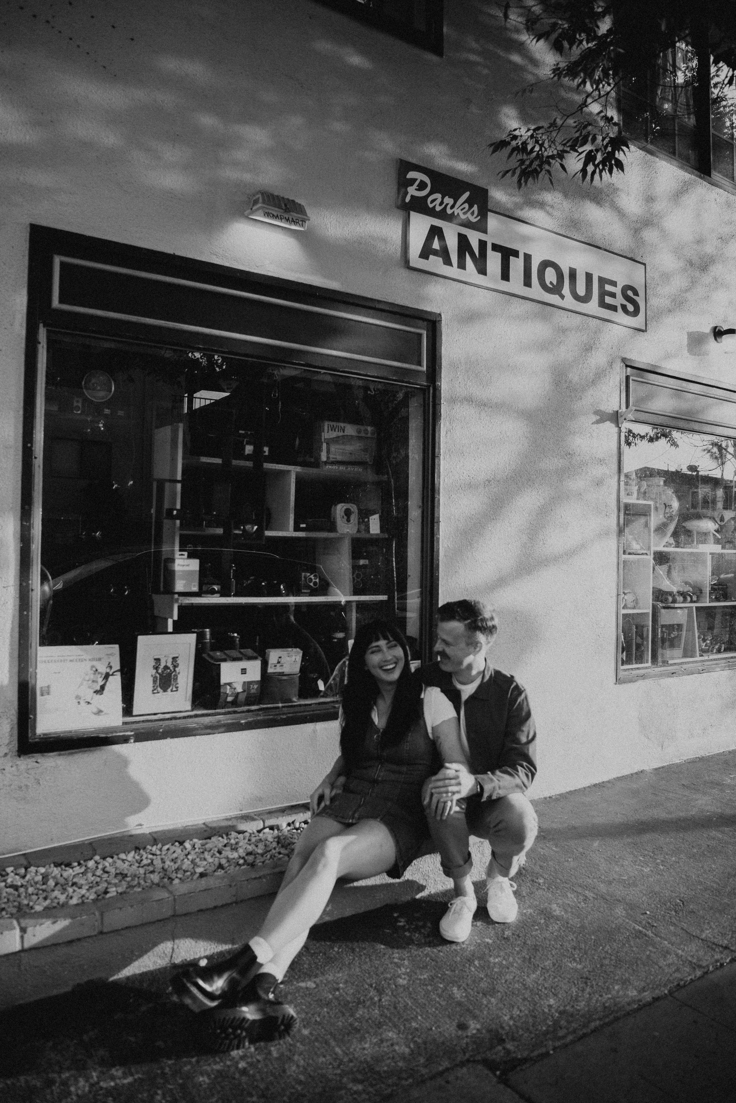 black and white photo of couple siting and laughing on the sidewalk in Long Beach California
