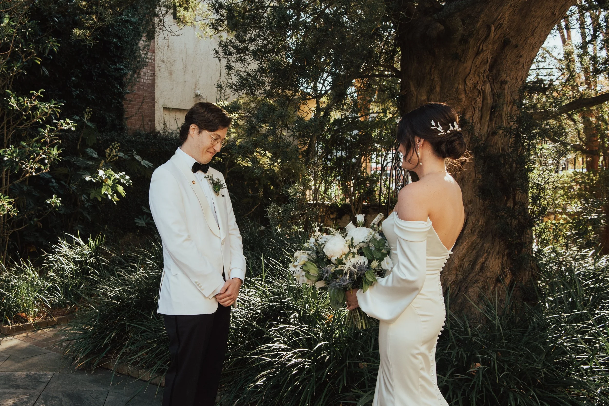 Bride and groom in front of a tree having their first look. Groom is emotion as he takes in his bride