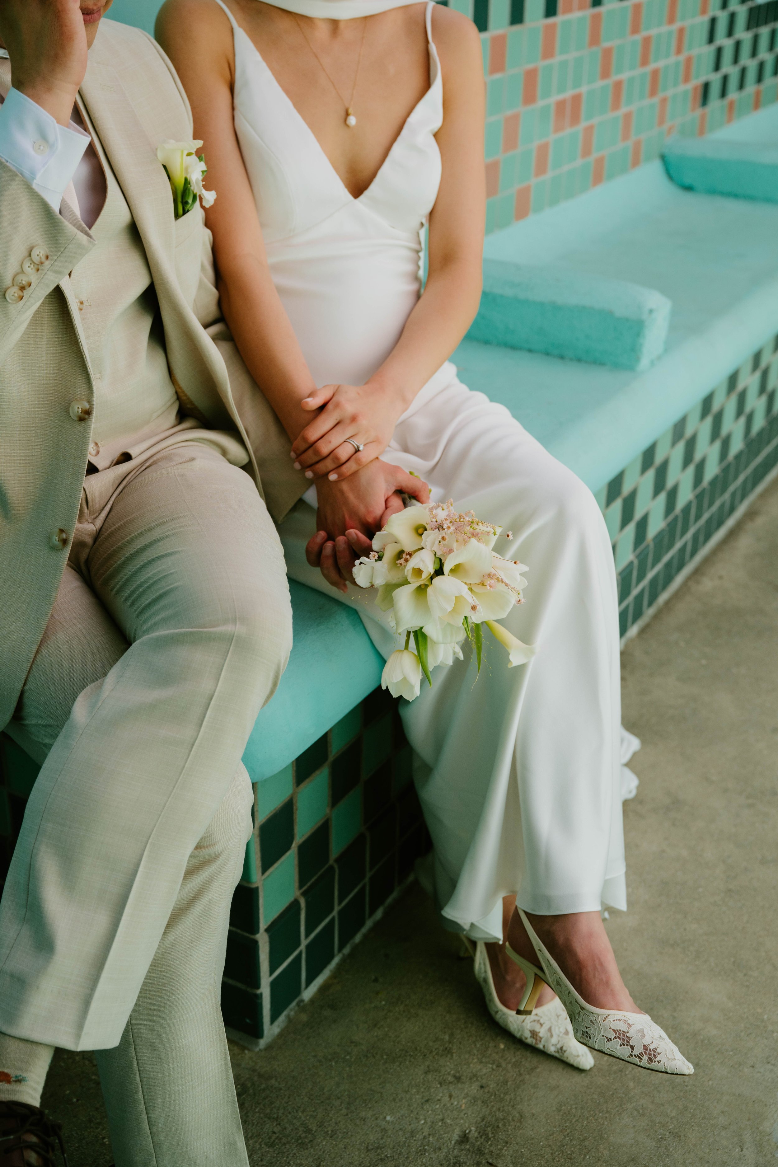close up of Bride and groom holding hands and the brides bouquet as they sit on a turquoise bench