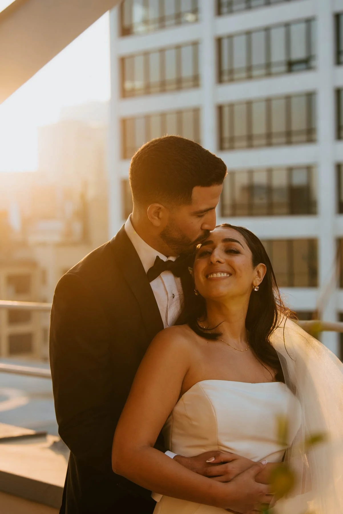 groom leaning down to kiss the forehead as she leans back into his chest.