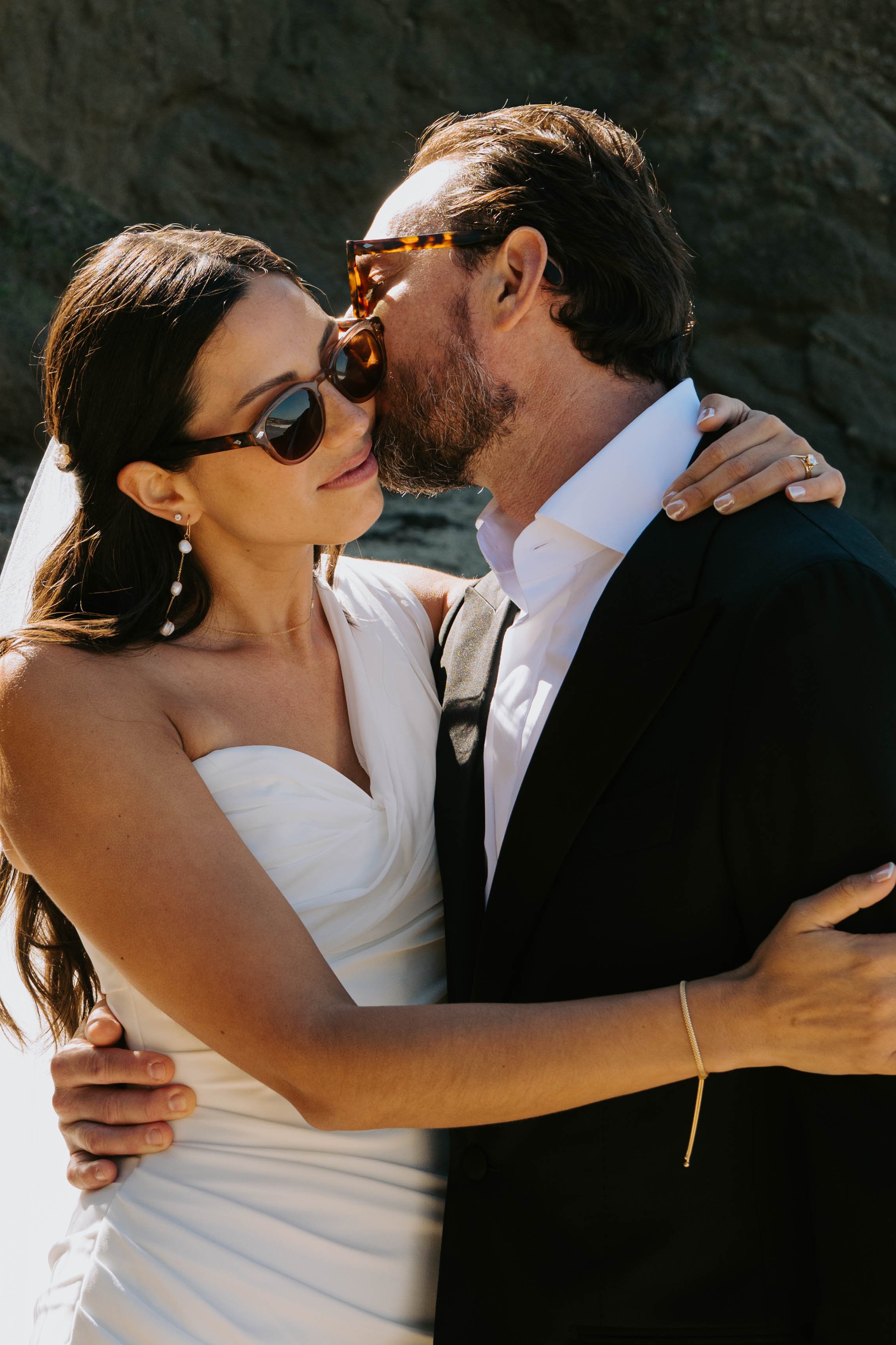 Groom kissing brides cheek. Both are wearing sunglasses