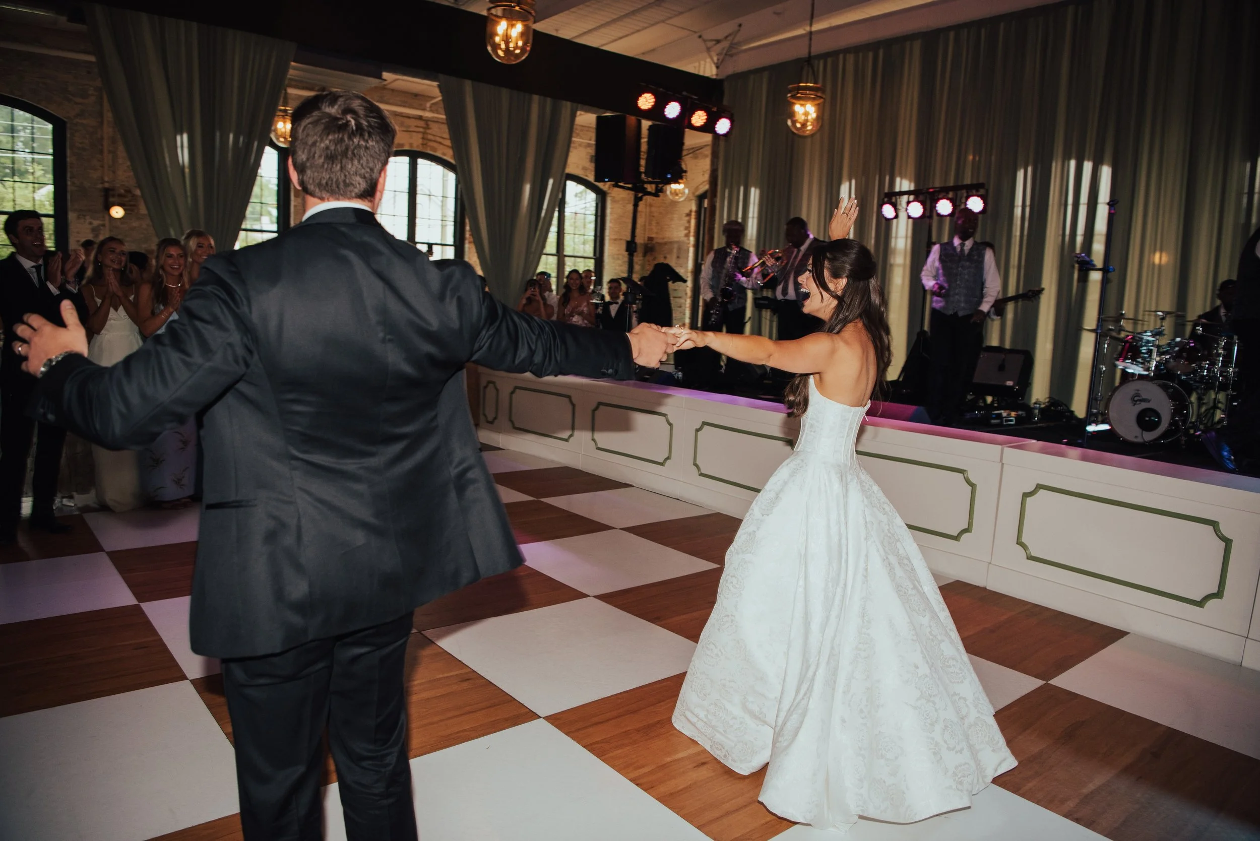 Bride and groom dancing on a wood and white checked dance floor with live band in the background