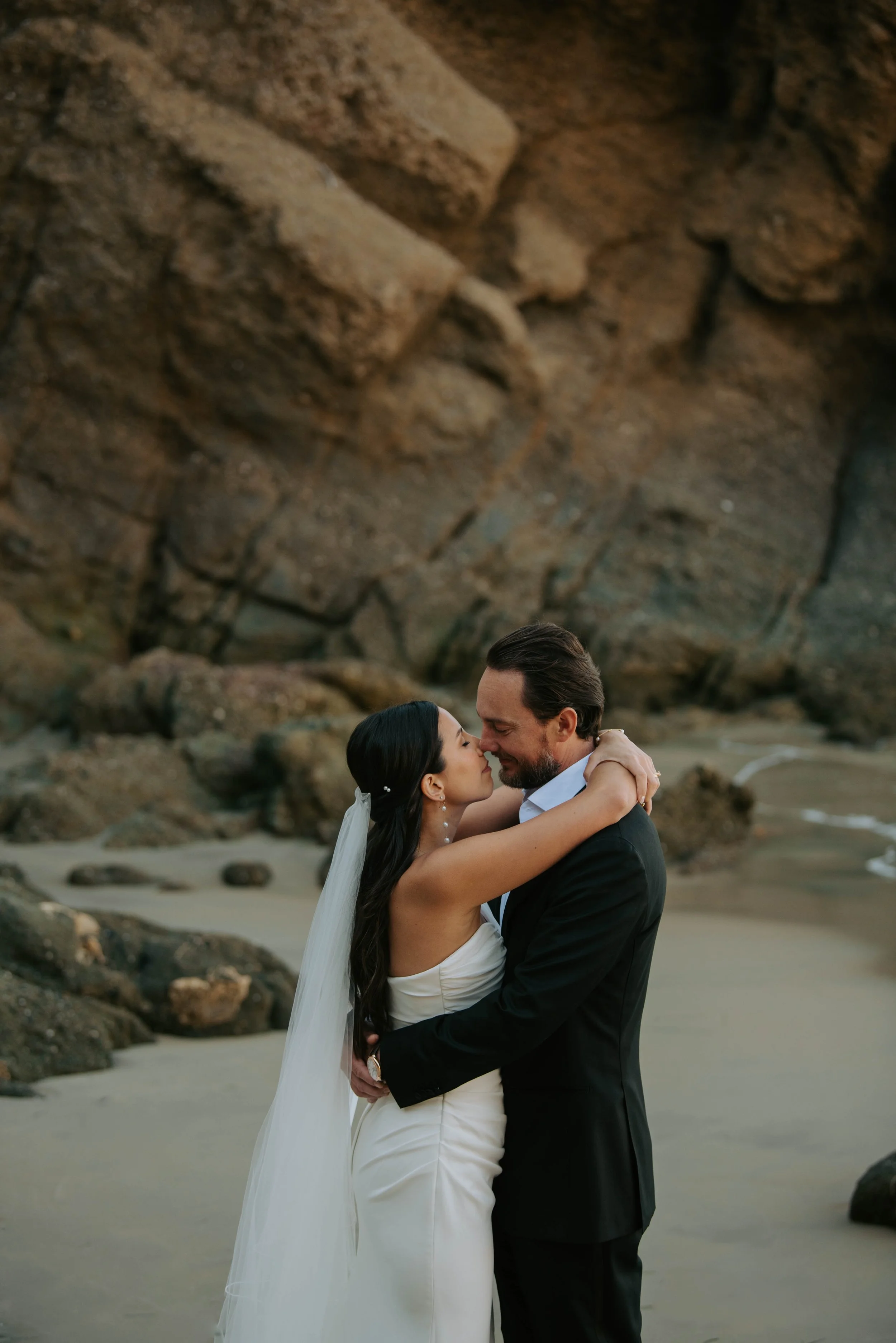 Bride and groom hugging on the beach with cliff in the background