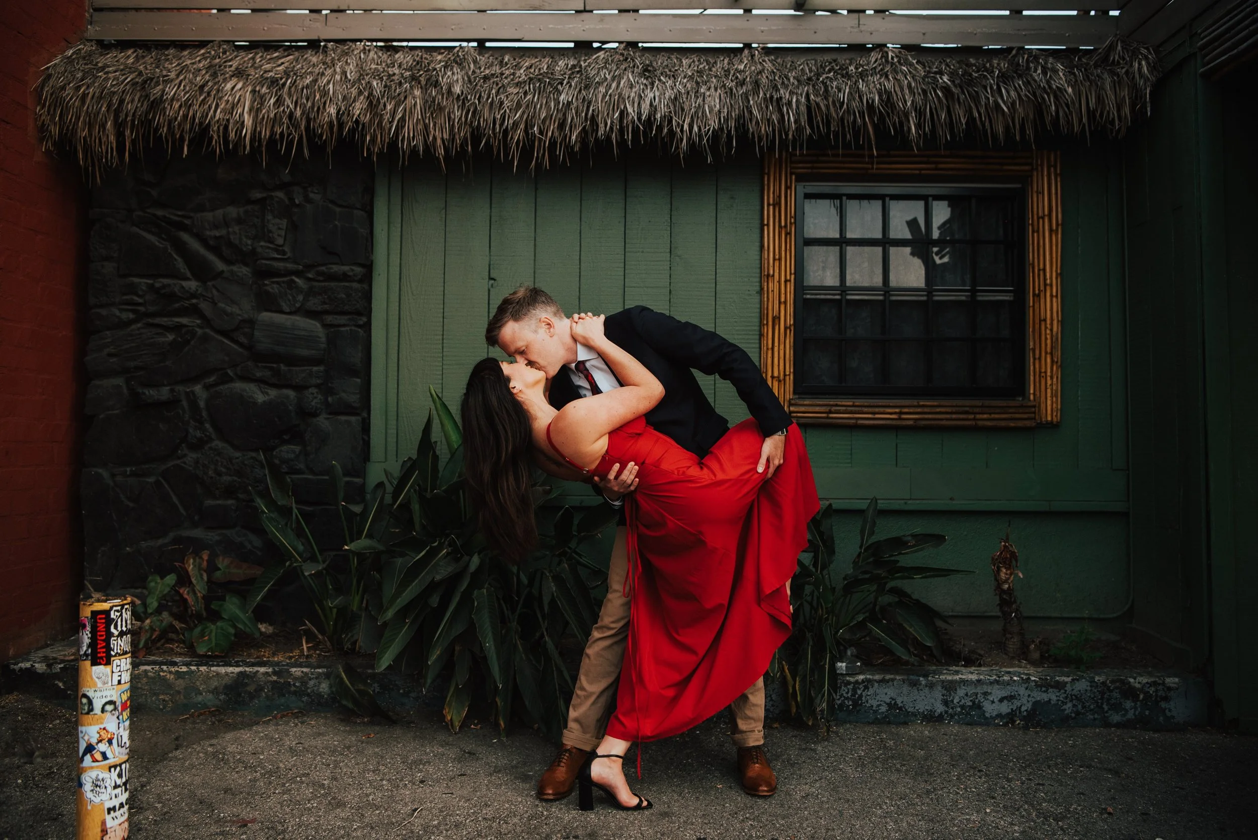 Guy dip kissing a girl in a red dress in front of a green wall
