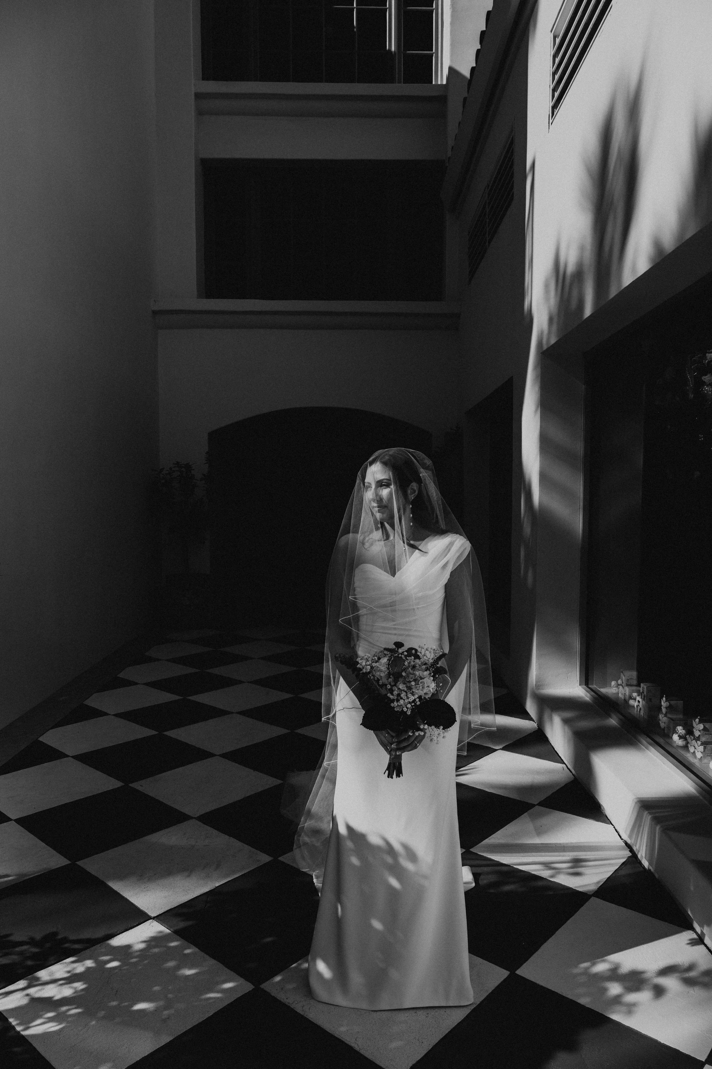 Black and White photo of Bride standing looking off to the side on a checkered Floor
