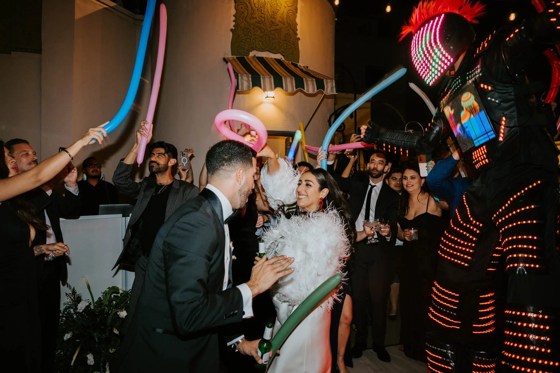 Bride and Groom dancing at night with guest waving balloons in the air and a giant robot dancing next to them