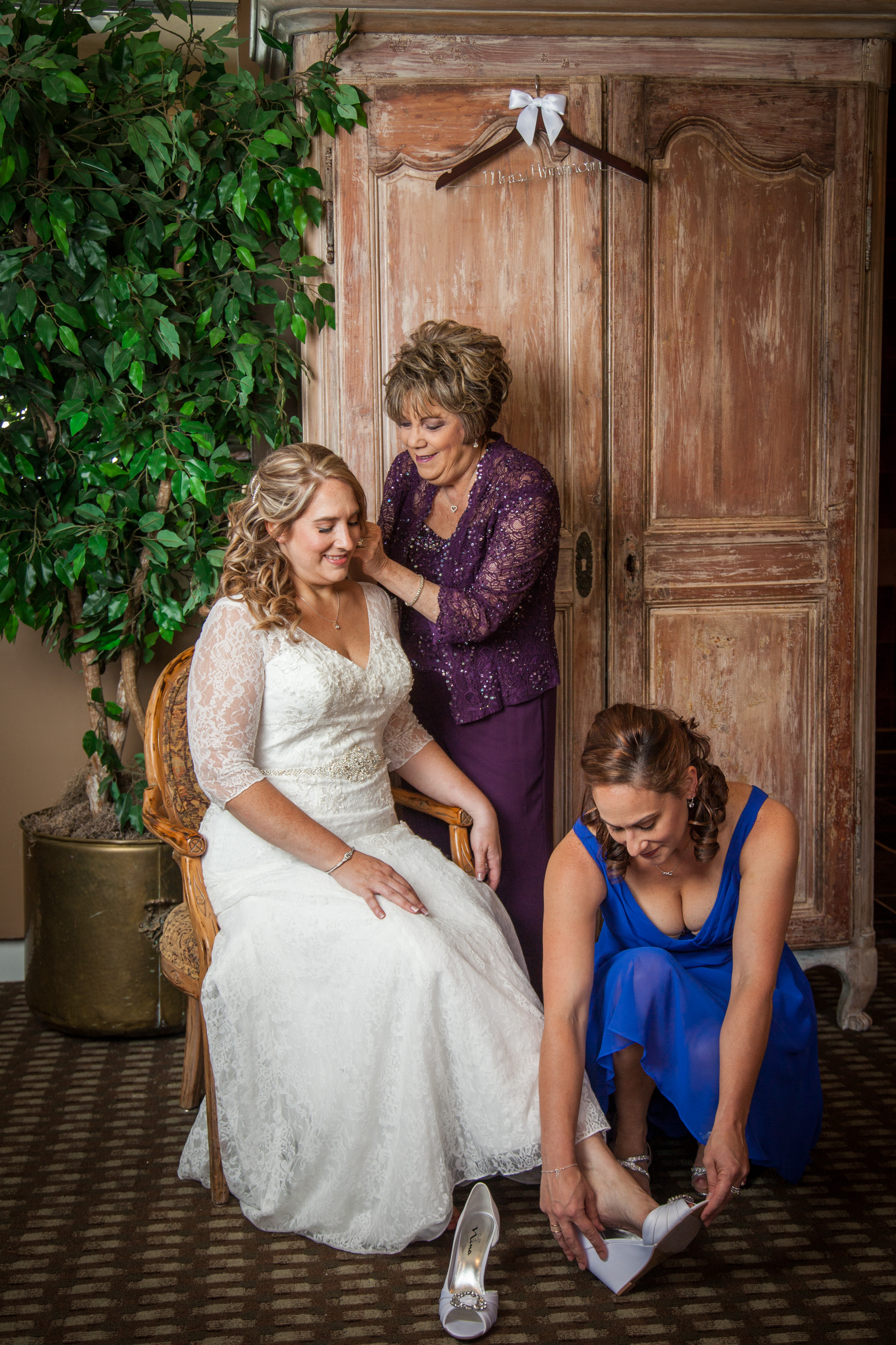 The beautiful bride in a white lace wedding gown gets ready for the ceremony with the help of her mother and sister.