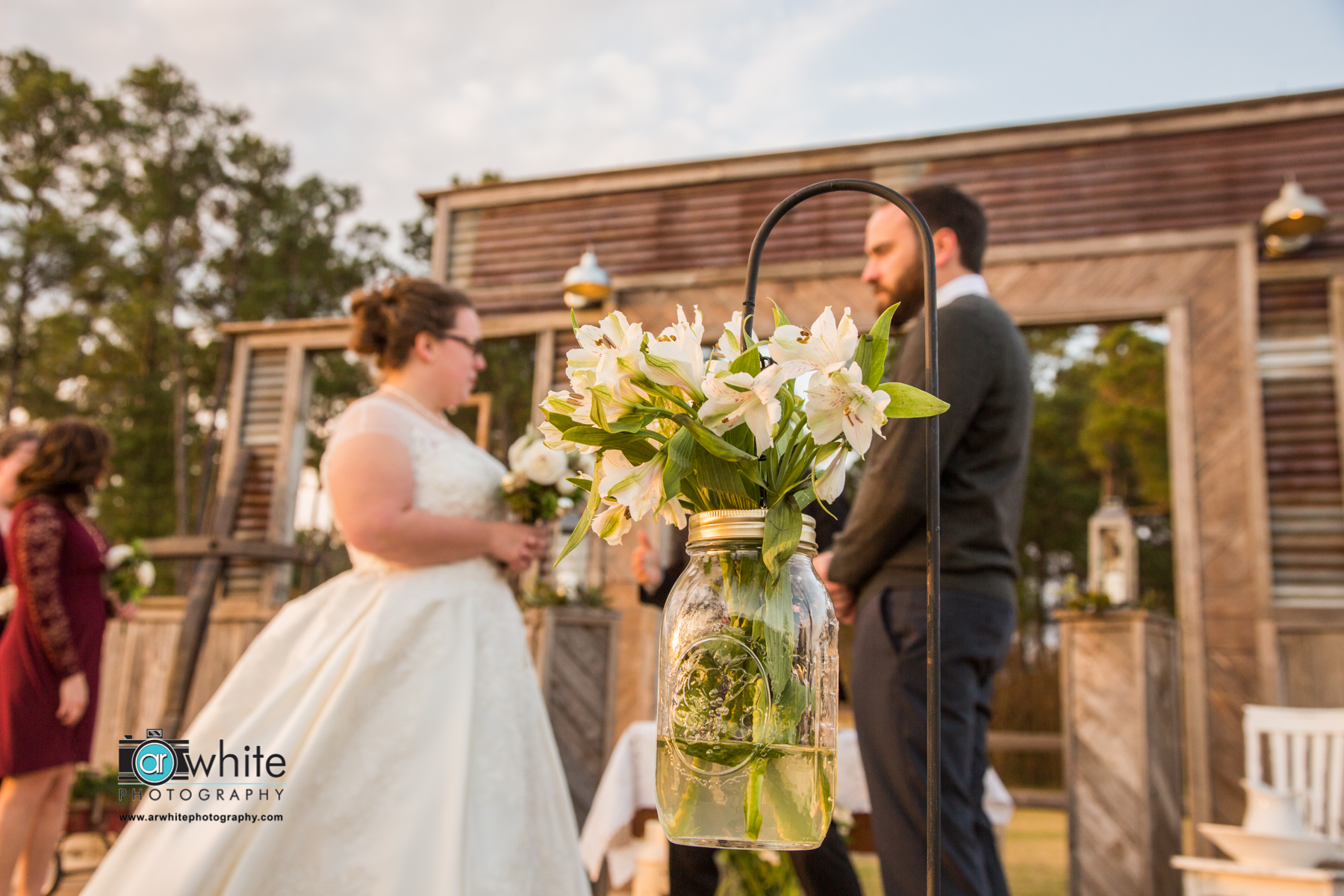 A mason jar with white flowers is used at a barn wedding for isle decoration at the alter. 
