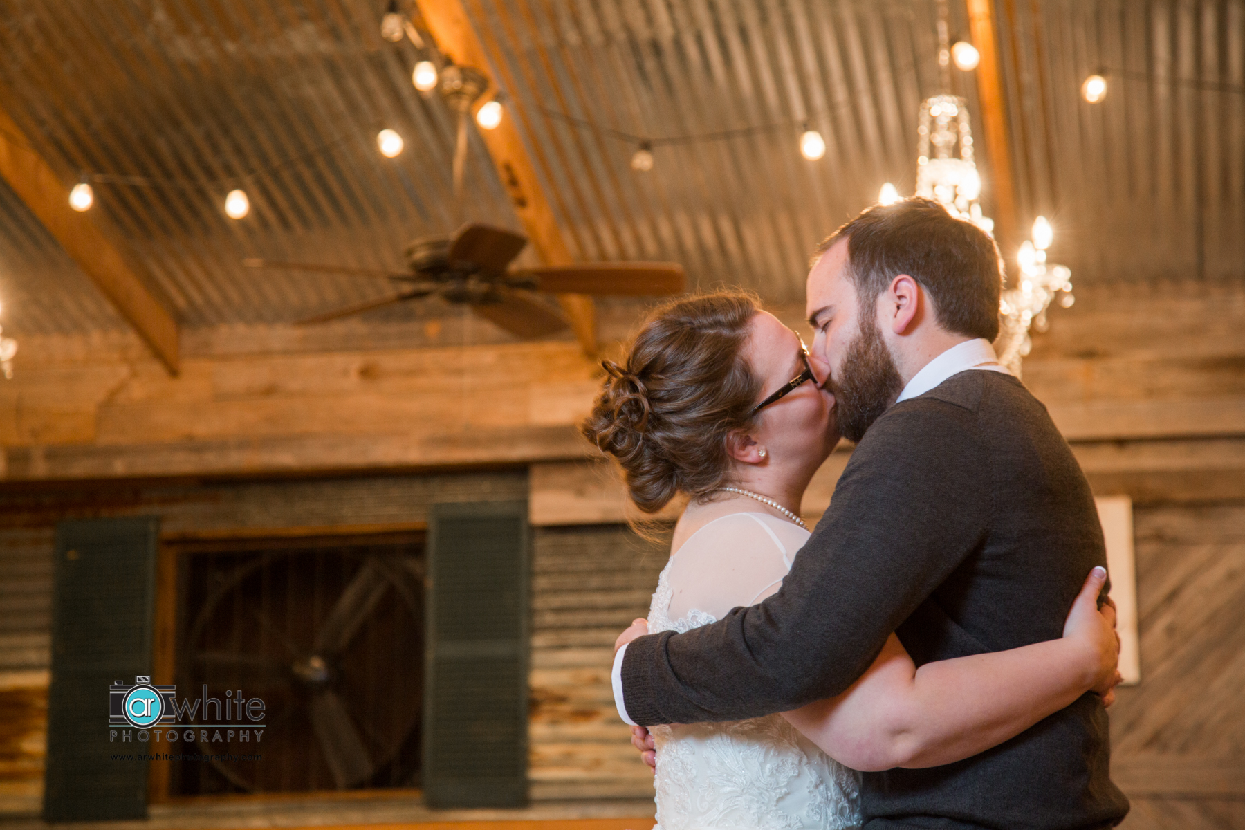 Husband and wife kiss after their first dance during the reception at a barn wedding.