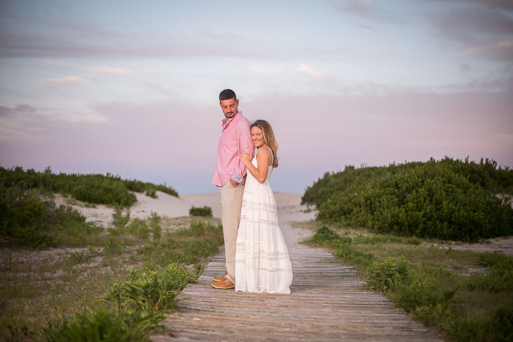 Engagement portrait of a man wearing a pink shirt with tan pants and woman wearing a white dress on the beach at Assateague taken by wedding photographers in Baltimore ARWhite Photography (Copy)