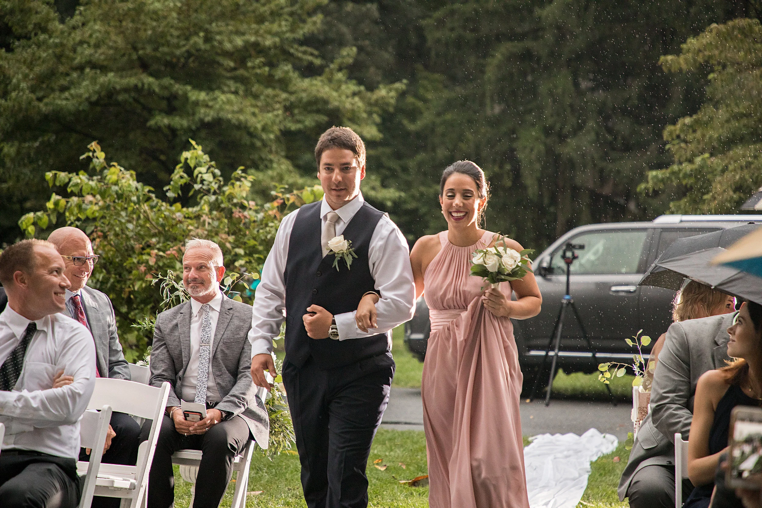 Rain falls as the maid of honor and best man walk down the isle.