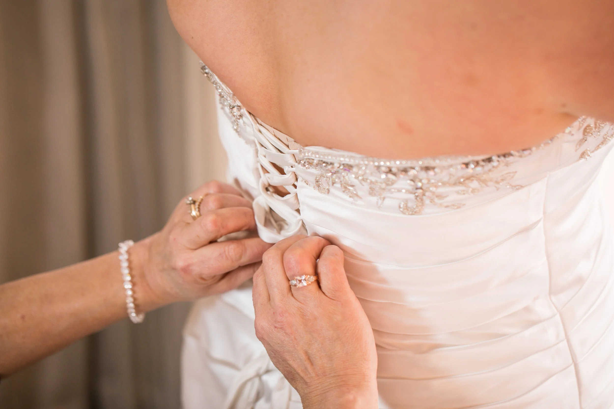 The mother of the bride helps Jenna get into her white elegant wedding gown before the start of the wedding.