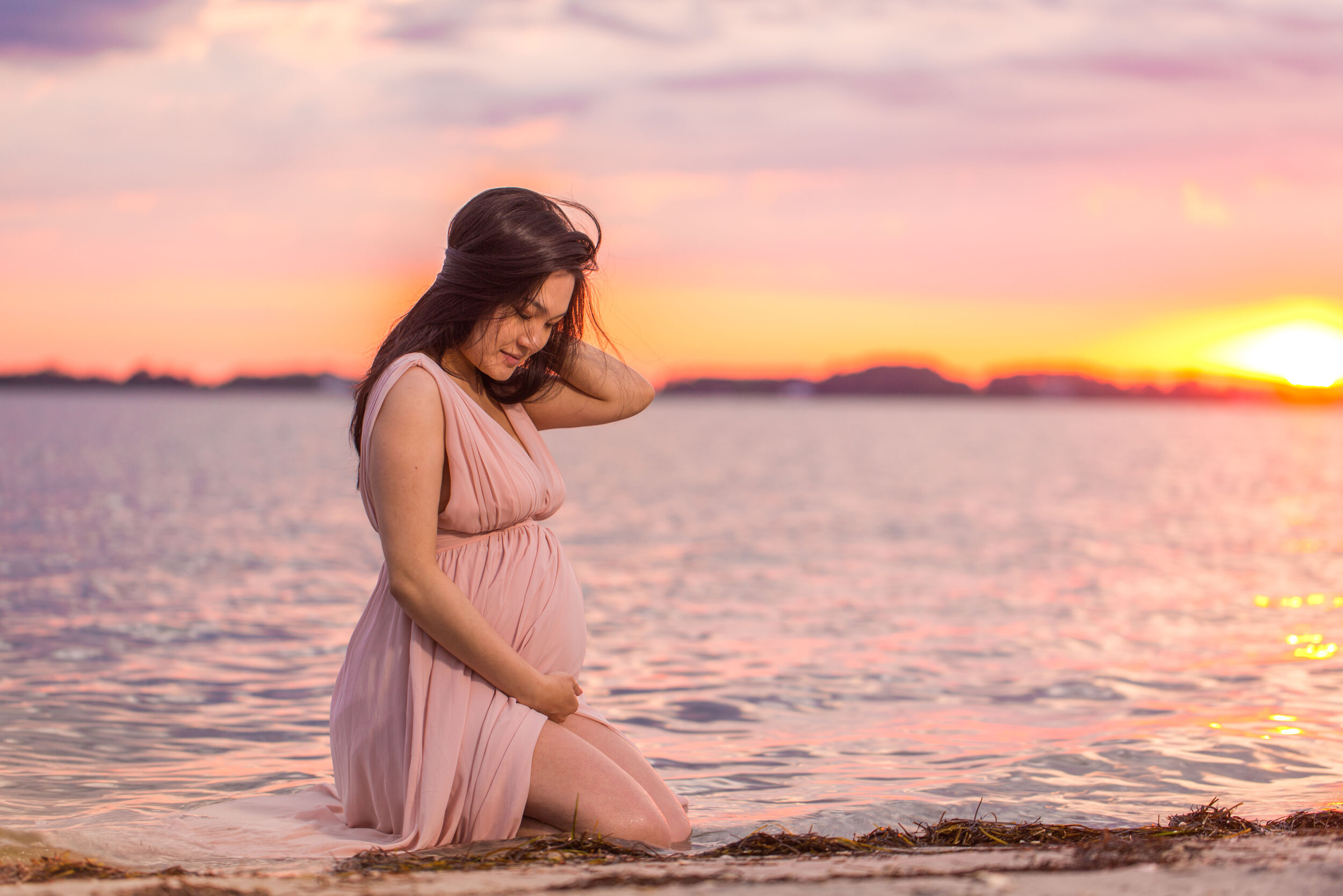 Photo of a pregnant woman in long flowy pink dress in the the water on the Assateague beach during her OCMD maternity session taken by photographers in Ocean City Maryland ARWhite Photography. (Copy)