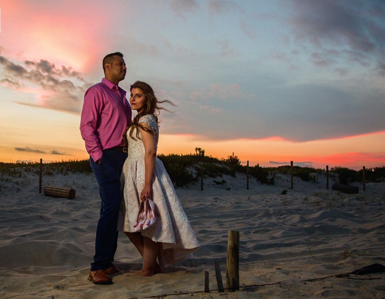 Engagement portrait of a man wearing a pink shirt with blue pants and his fiance wearing a white dress on the beach at Assateague taken by wedding photographers in Baltimore ARWhite Photography (Copy)
