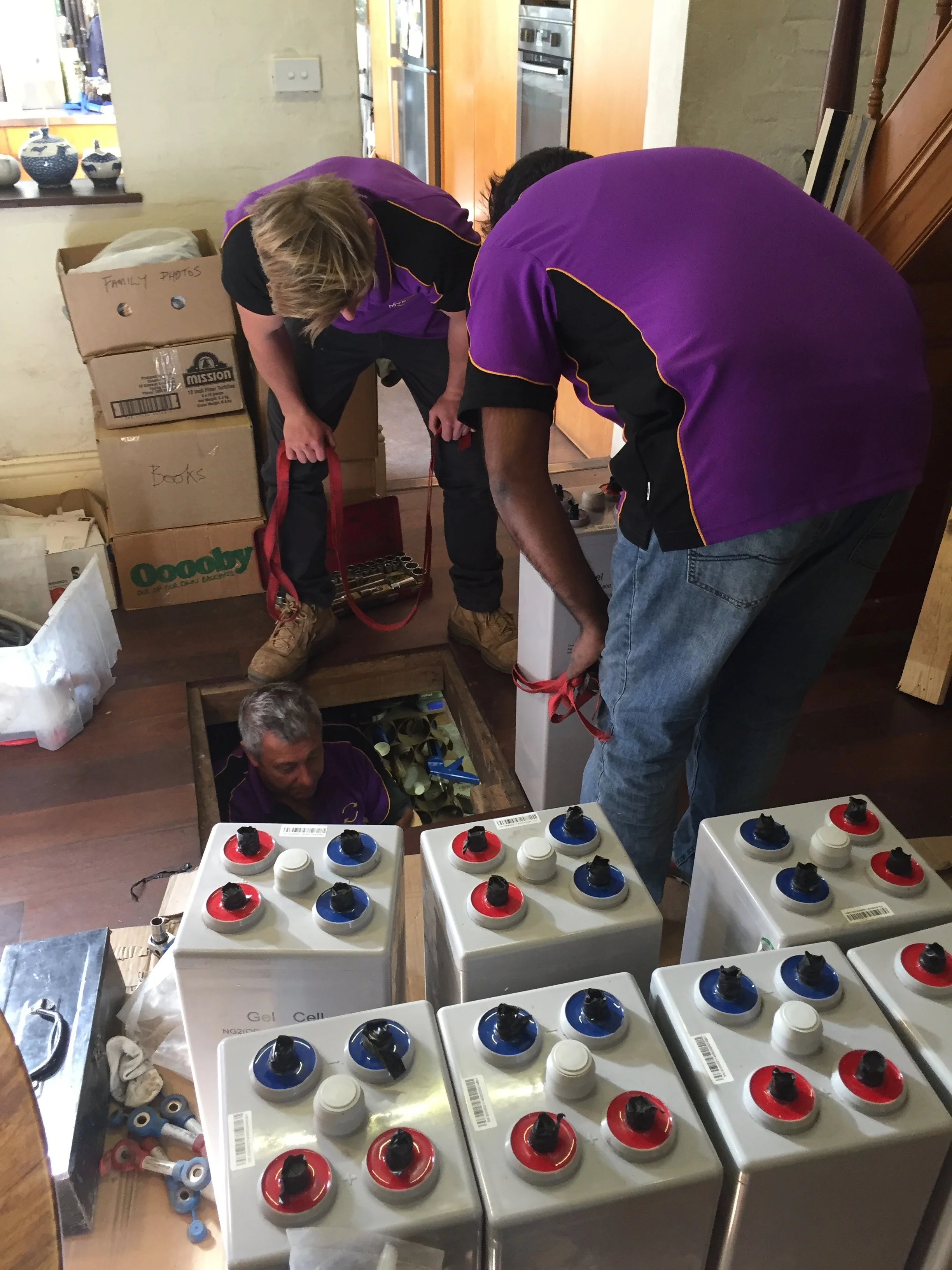 • Gel batteries on dining room floor with MV Solar workers lowering batteries to Michael in the cellar