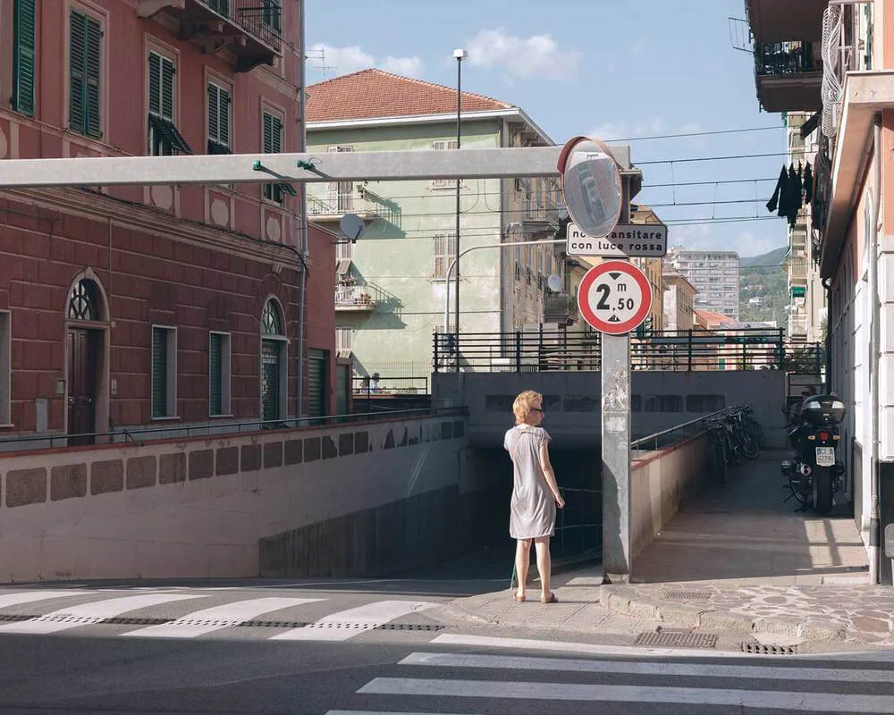 A woman standing at a street corner near an underwater pedestrian tunnel entrance in an urban area with buildings and parked bikes.