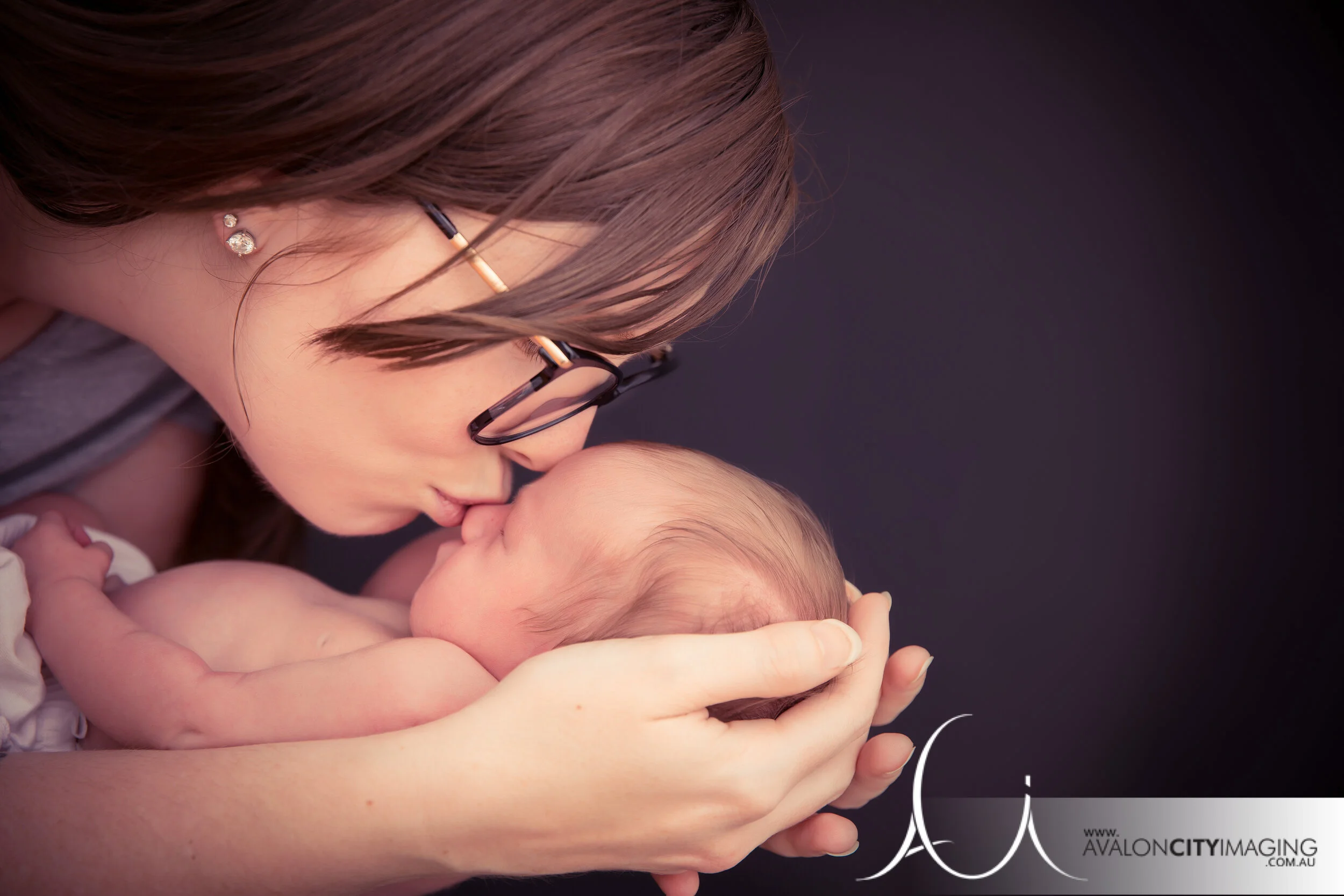 newborn photography - newborn in mum's arms with a soft kiss on the nose warm studio lighting.jpg