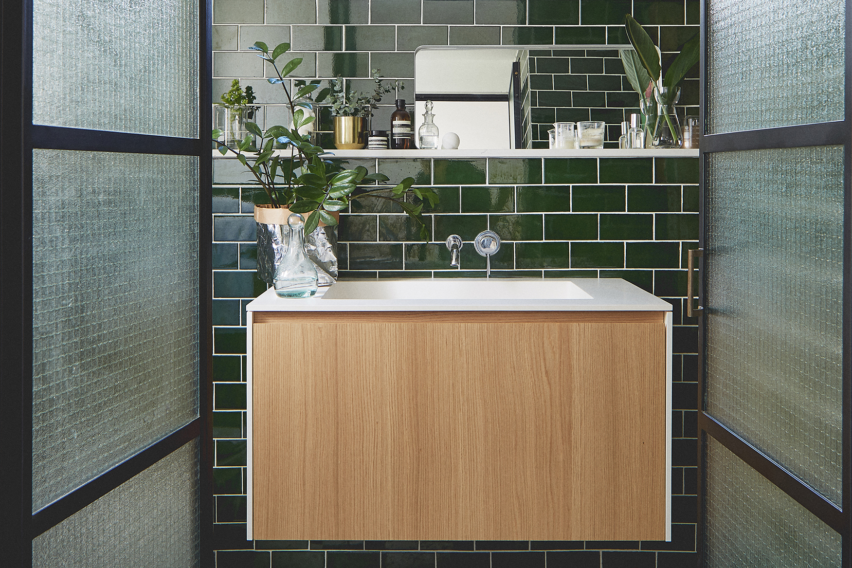 Steel frame doors bathroom emerald green tiles plants and cosmetics corian sink