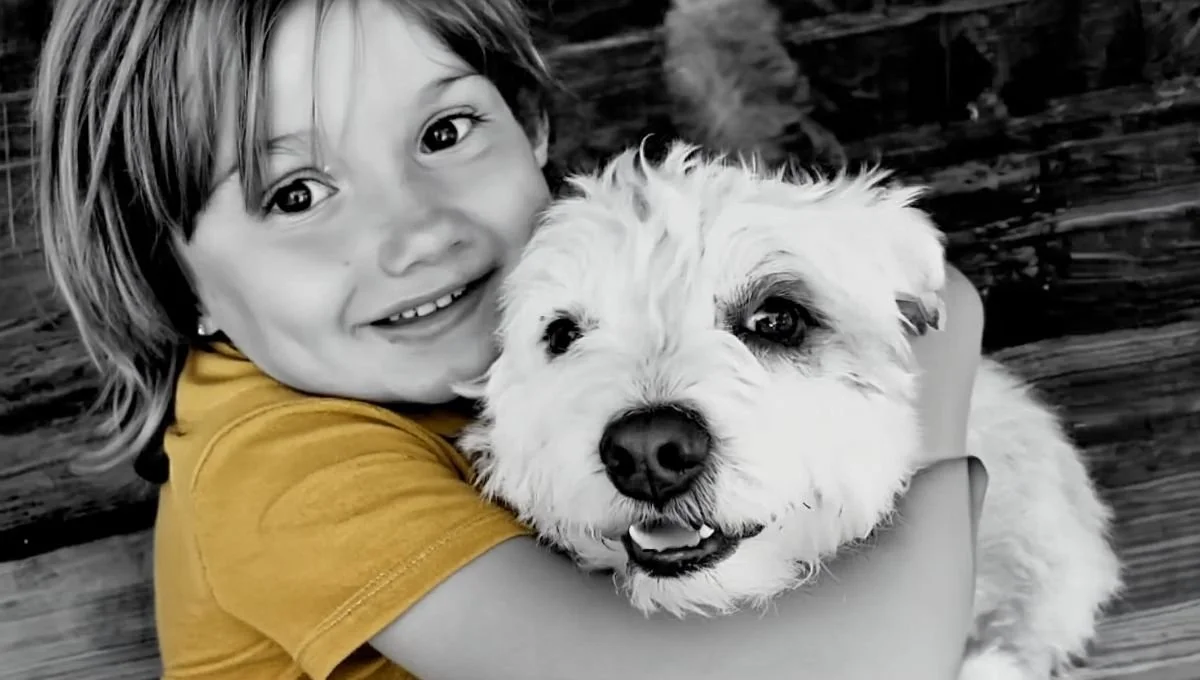 Enfant souriant tenant un petit chien blanc dans ses bras.
