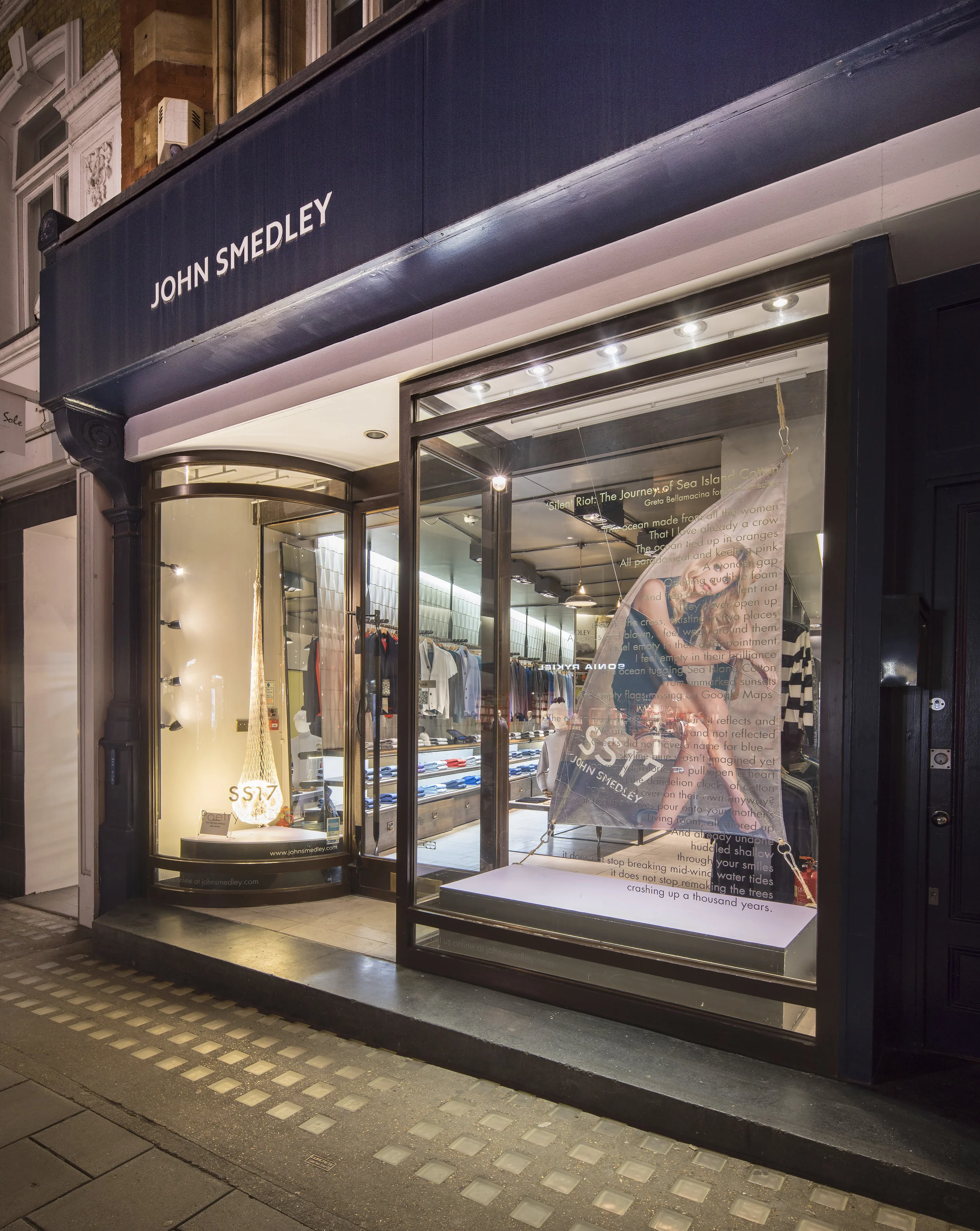 SS17: Poetry of Colour Drawing inspiration from Greta Bellamacina's poem 'Silent Riot: The Journey of Sea Island Cotton' written for John Smedley we added a nod to the nautical to the SS17 window display. In the main window Greta's image was printed onto a sail shaped canvas secured in place with hessian ropes, carabiners and positioned behind a window vinyl displaying her poem. The secondary window features a fishing net containing an illuminated ball representative of a water droplet to create an eye-catching focal point for passers-by. Inside the store, continuing the nautical theme, point-of-sale features Greta’s image printed onto canvas and stretched into frames while swing tickets are printed onto canvas and hung using the same hessian rope as the window.