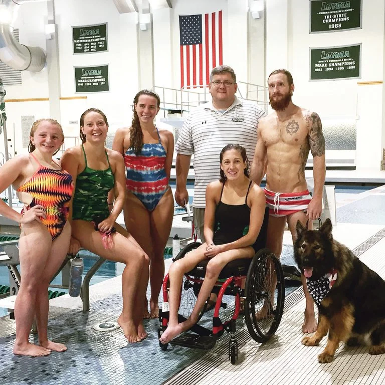 Five members of Team USA train together under Coach Brian Loeffler, ’91, at the Mangione Aquatic Center at Loyola University Maryland: (pictured left to right) McKenzie Coan, ’18, Cortney Jordan, M.A.T. ’16, Elizabeth Smith, Loeffler, Alyssa Gialamas, ’18, and Navy veteran Brad Snyder and his service dog, Gizzy (photo courtesy of Loyola Athletics).