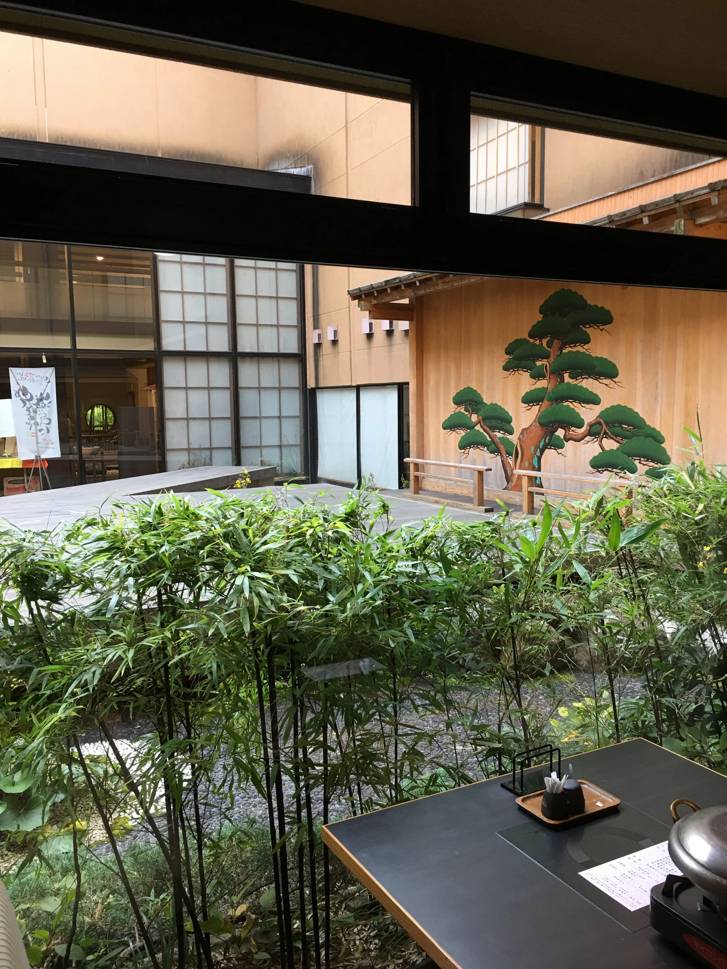 The restaurant presents itself with settings from both modern and traditional styles of Japanese display. Edo-like fashioned Japanese black pine is painted on the smooth wooden surface beyond the transparent glass wall. More of the restaurant table and the left side of the open area view beyond the glass barrier photo is shown: here .