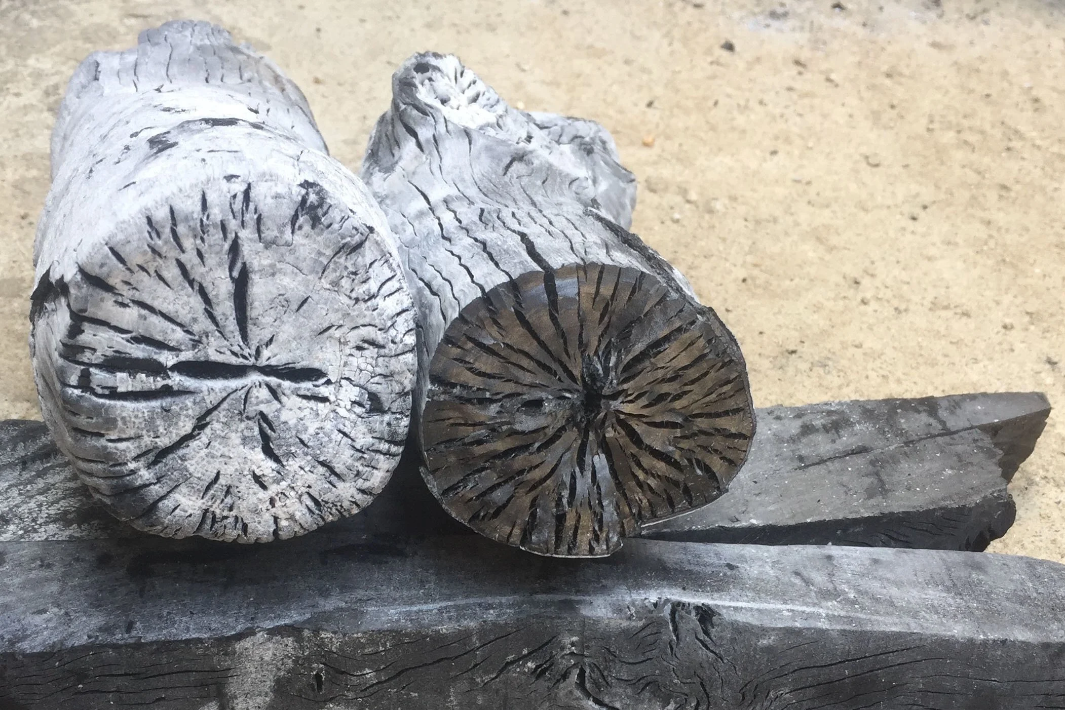 Two large pieces of uncut white lychee wood charcoal, set on a wood surface against a sandy background in Vietnam.