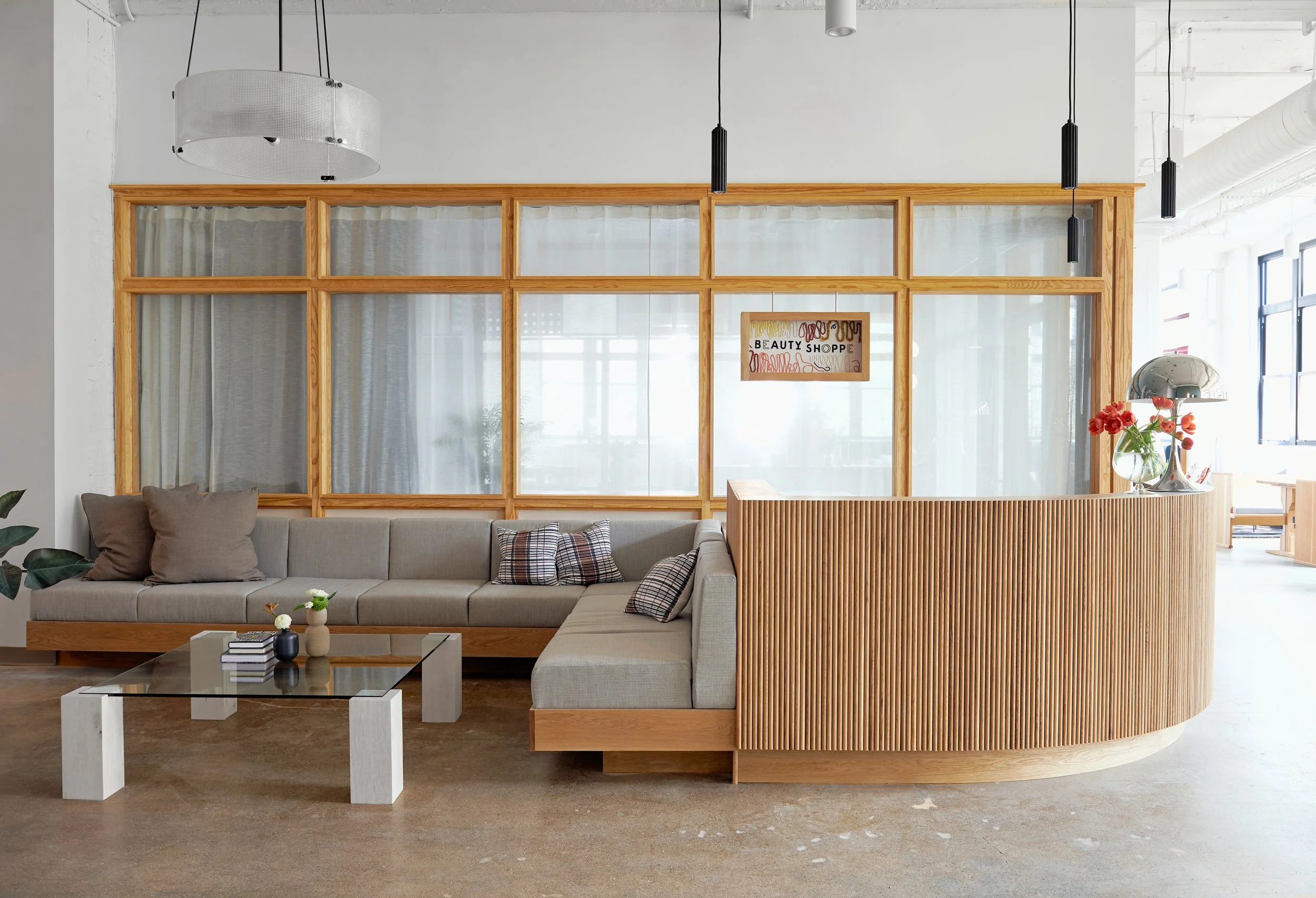 Custom white oak tambour curved reception desk with integrated upholstered sofa seating; birdseye maple pillar leg coffee table with inset tempered glass top; embroidered sign.