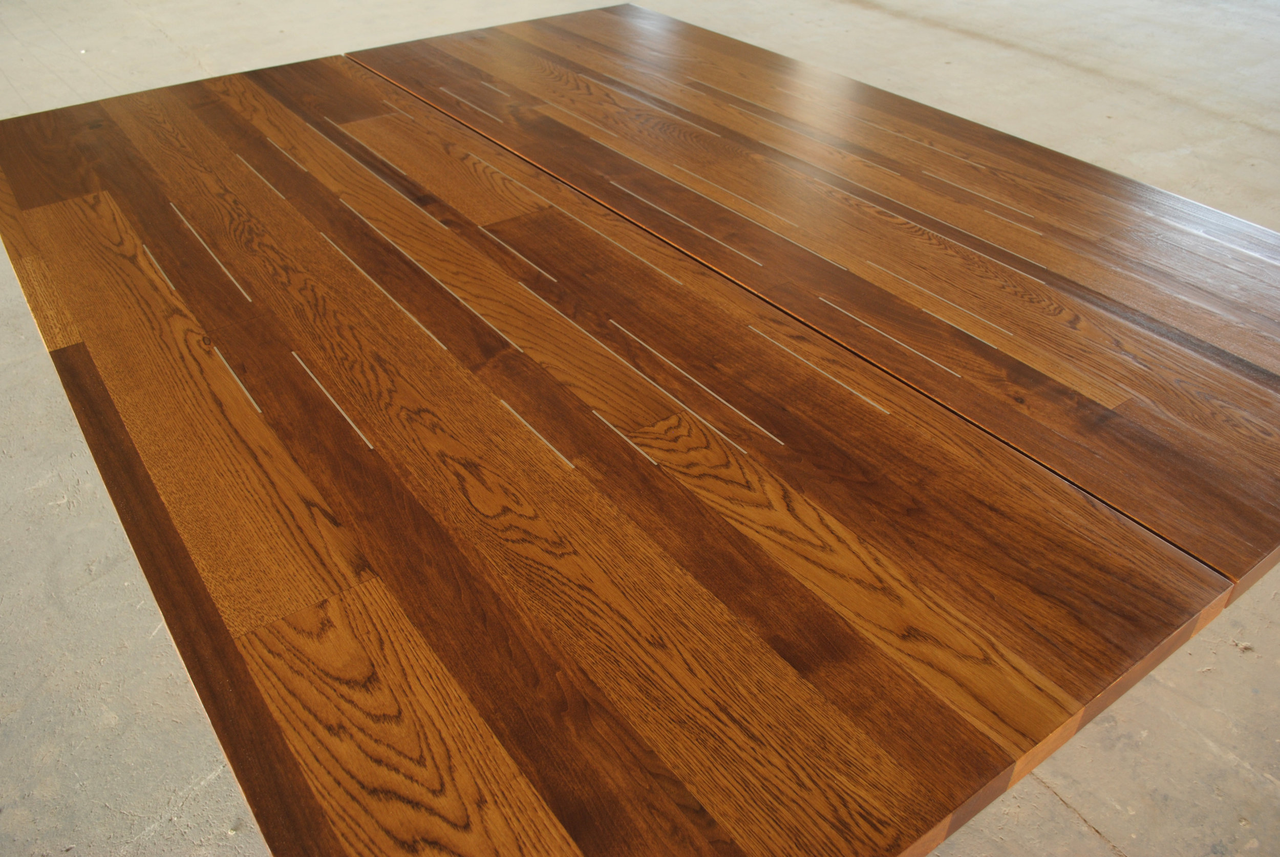 Inlay detail of custom oak and butternut dining tables with aluminum bar inlay and trestle legs.