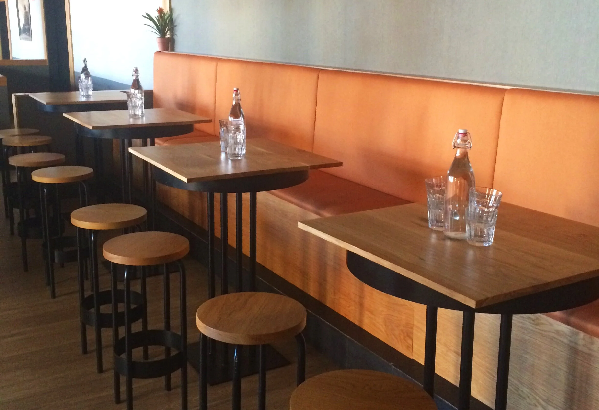 Custom white oak and steel high top dining tables, stools, and upholstered banquette seating..