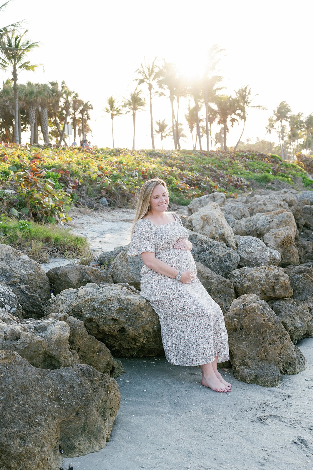 pregnant mom sitting on rocks at Dubois Park in Palm Beach with sunset behind her