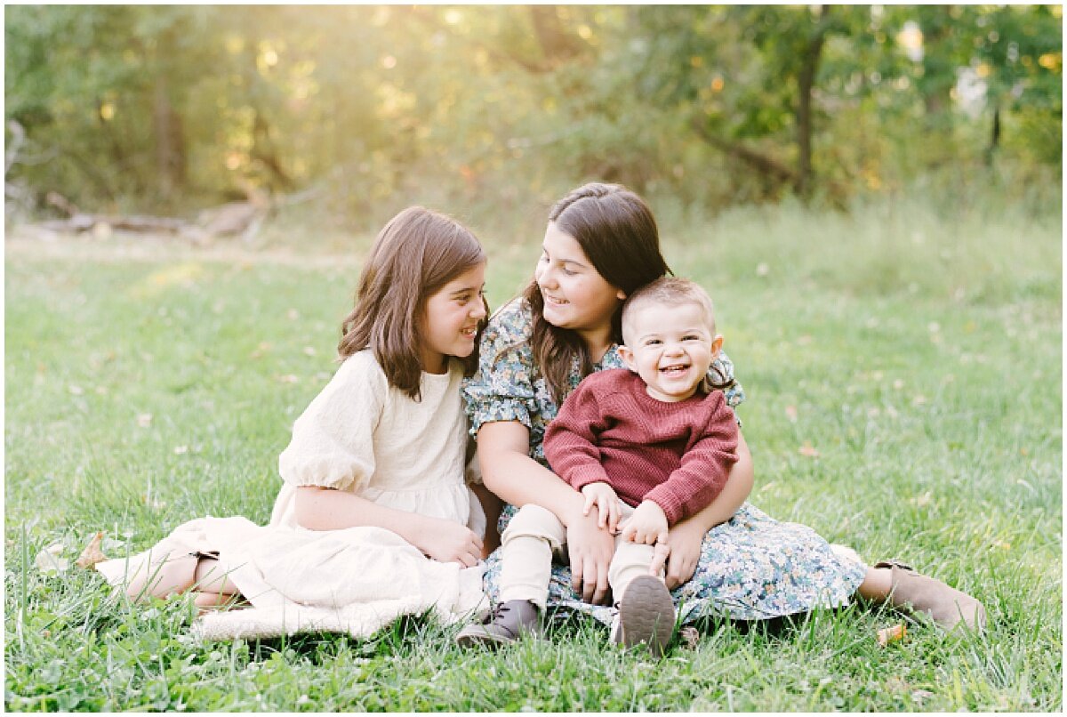  Smiling baby boy with with big sisters on the grass 