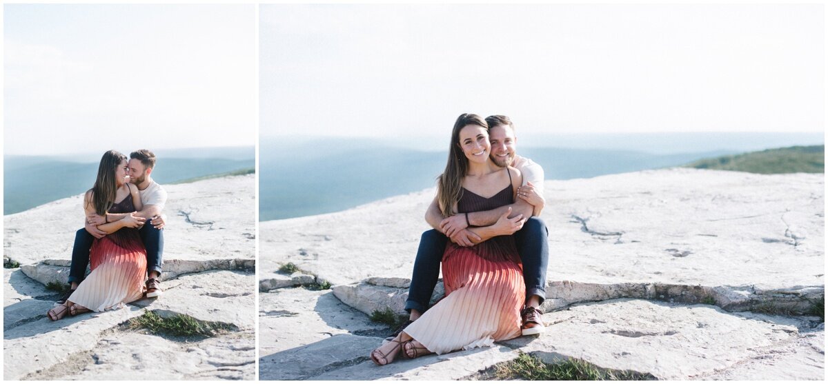 Man sitting behind woman while they're looking at each other | couple sitting on rocks during Minnewaska State Park engagement session | NKB Photo