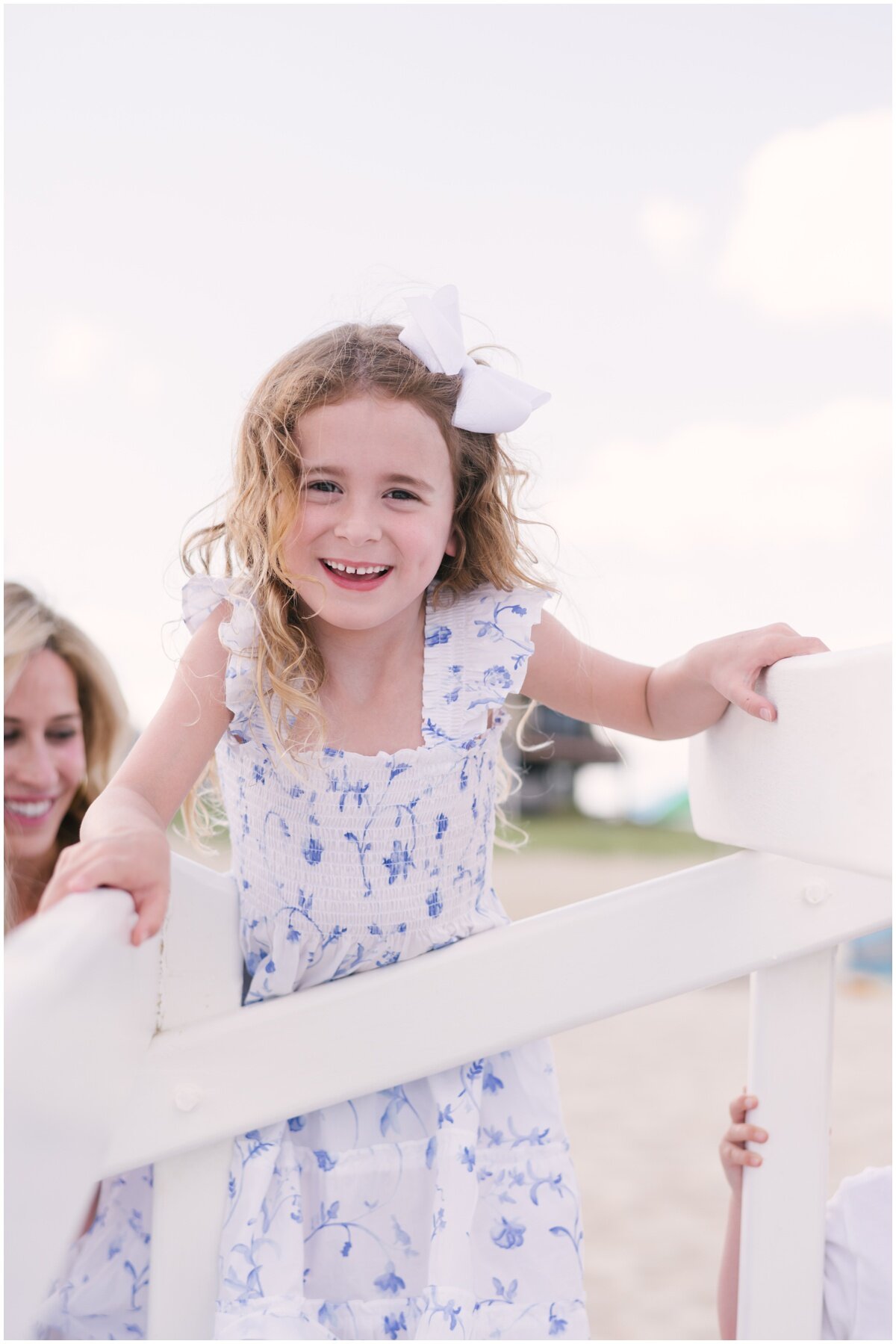 Girl wearing blue and white floral dress with white bow in hair during family beach session | NKB Photo