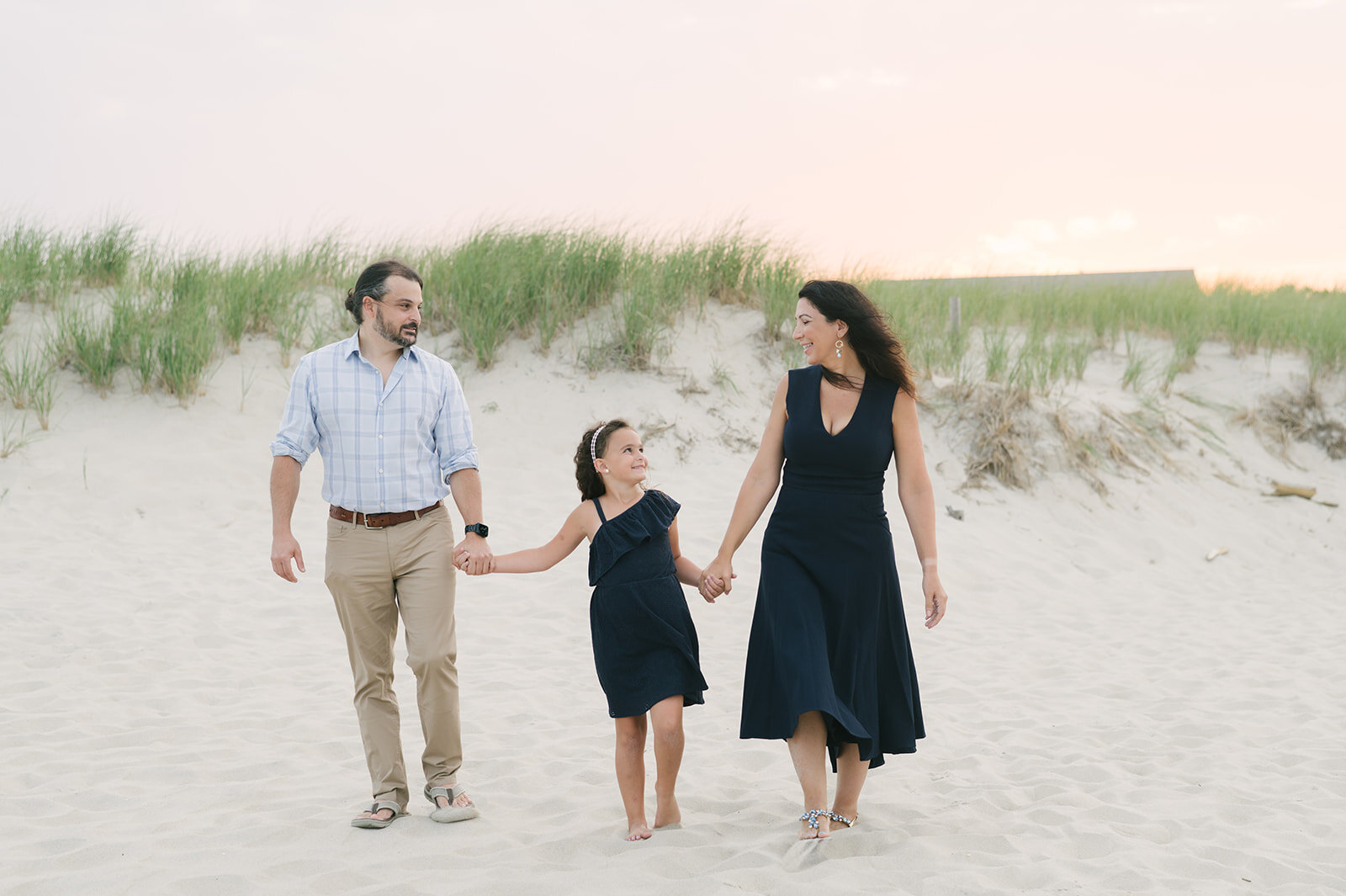 Mom, dad, and daughter holding hands and walking on beach during photos  | NKB Photo