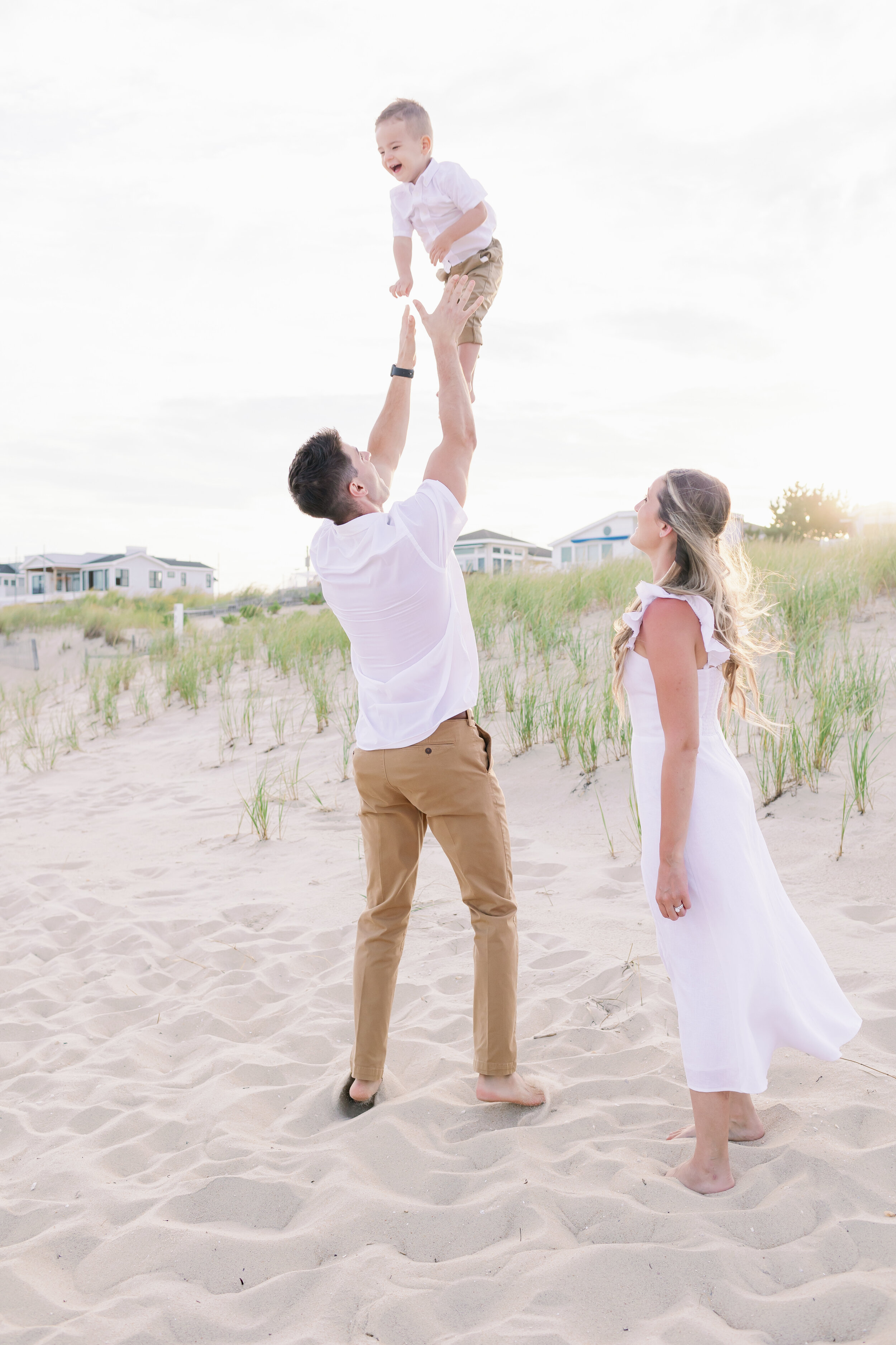 Dad throwing toddler in air while mom watches during beach photos | NKB Photo 