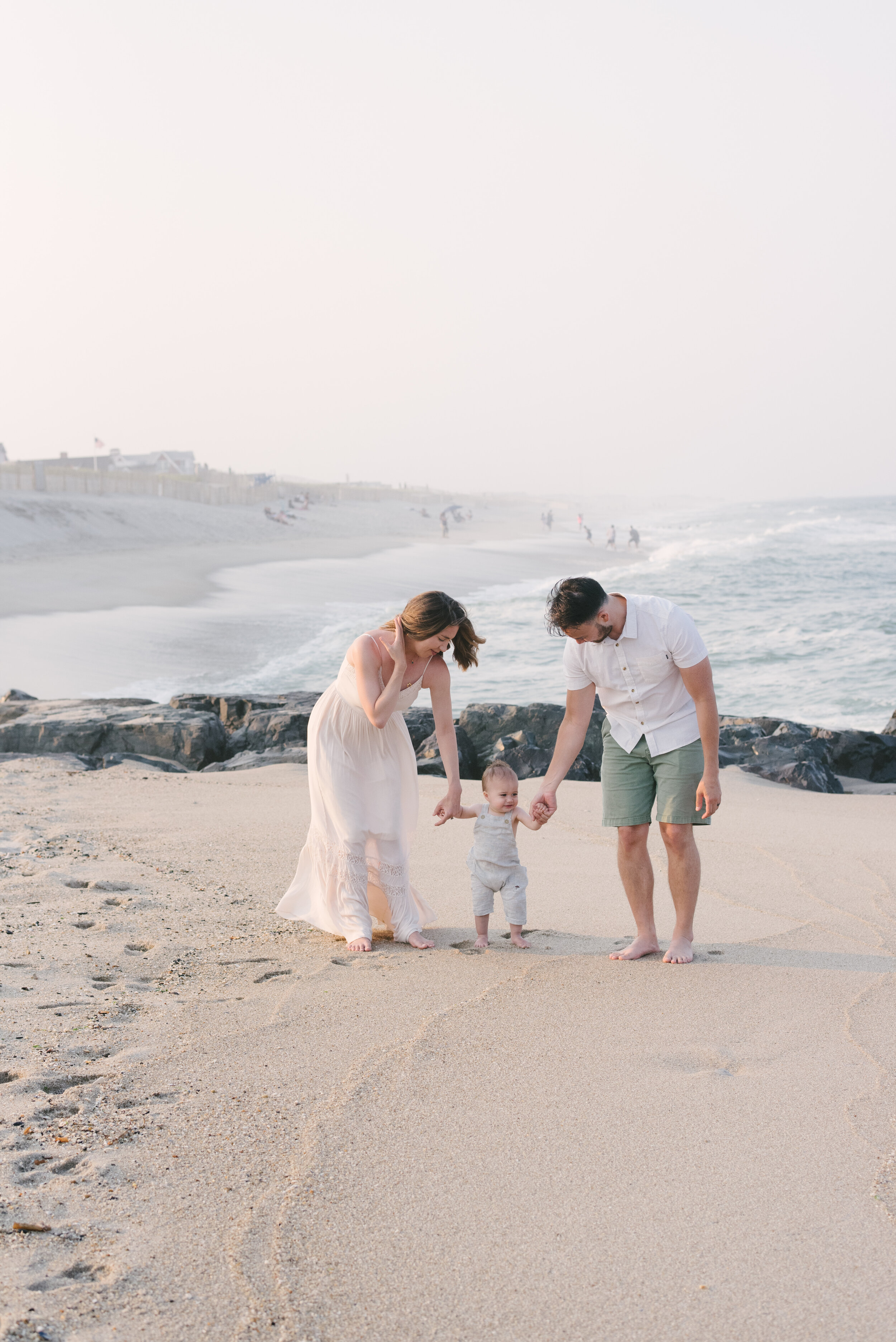 Beach photo ideas: Baby walking on beach while holding parents' hands | NKB Photo
