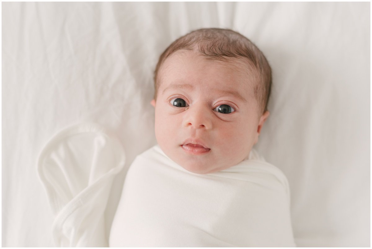 Newborn swaddled in white blank and looking at camera  during session with Jupiter photographer | NKB Photo